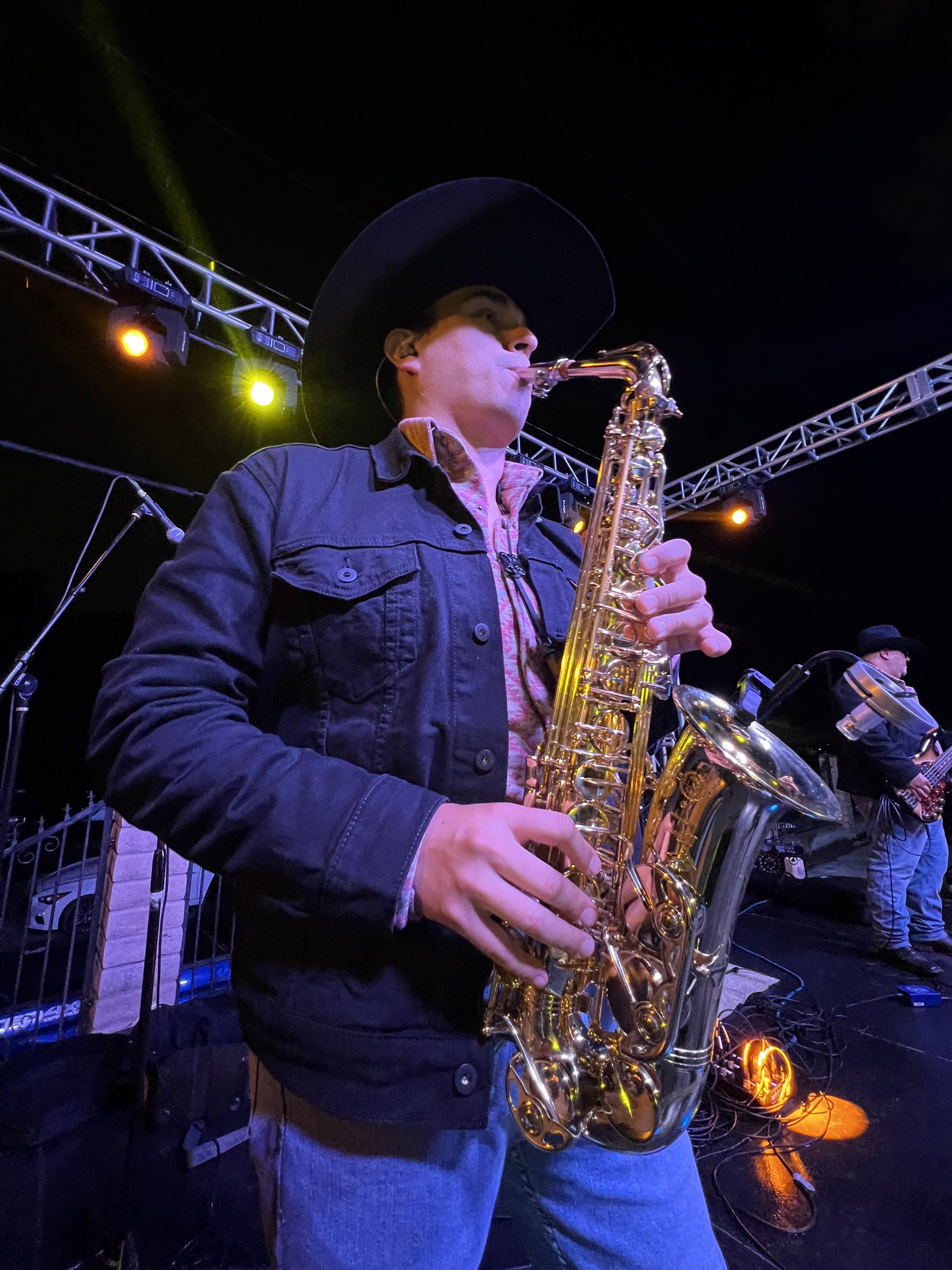 Hombre tocando saxofón en concierto nocturno, con luces de escenario y estructura metálica