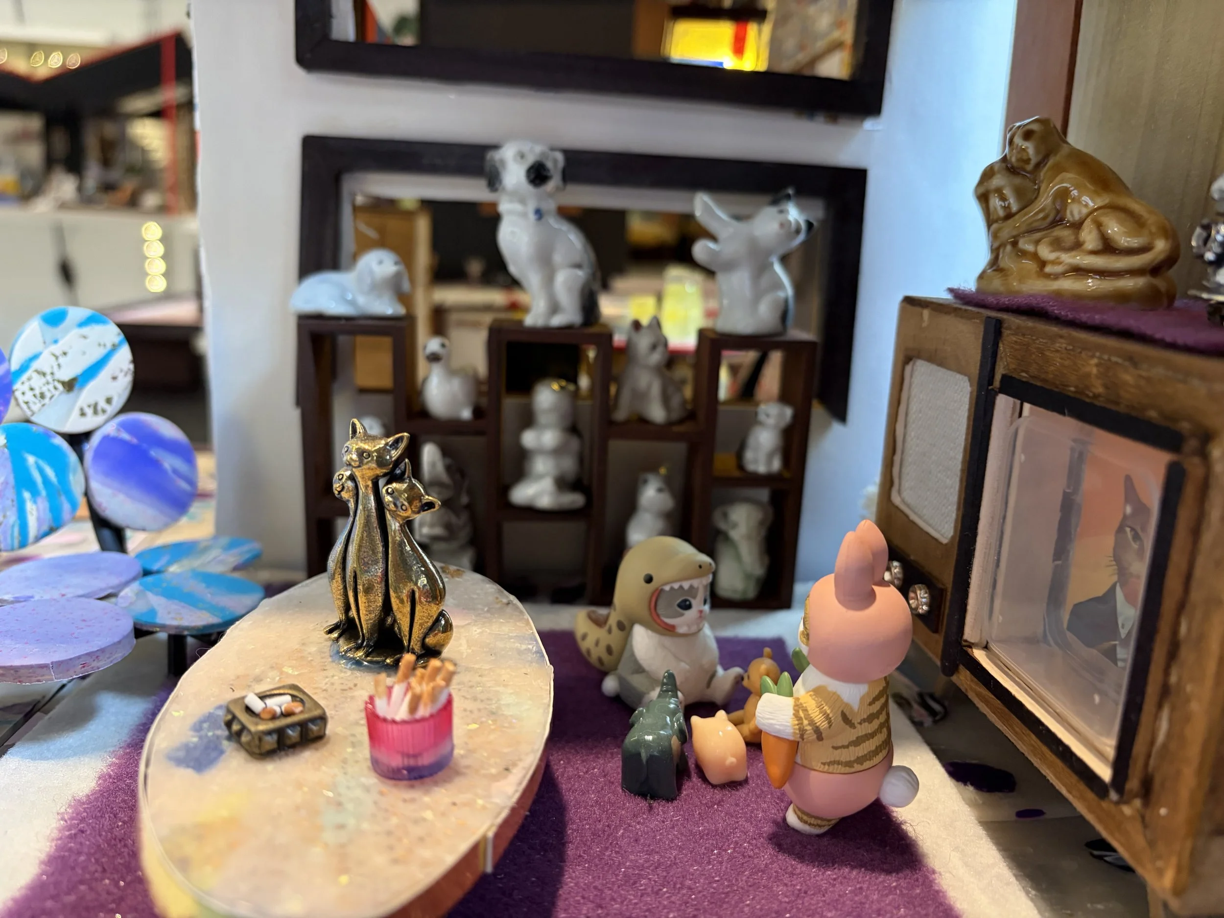 A small figurine of a gold-colored animal, possibly a dog, sitting on a speckled beige and pink surface, among various other small figurines and decorative items inside a store.
