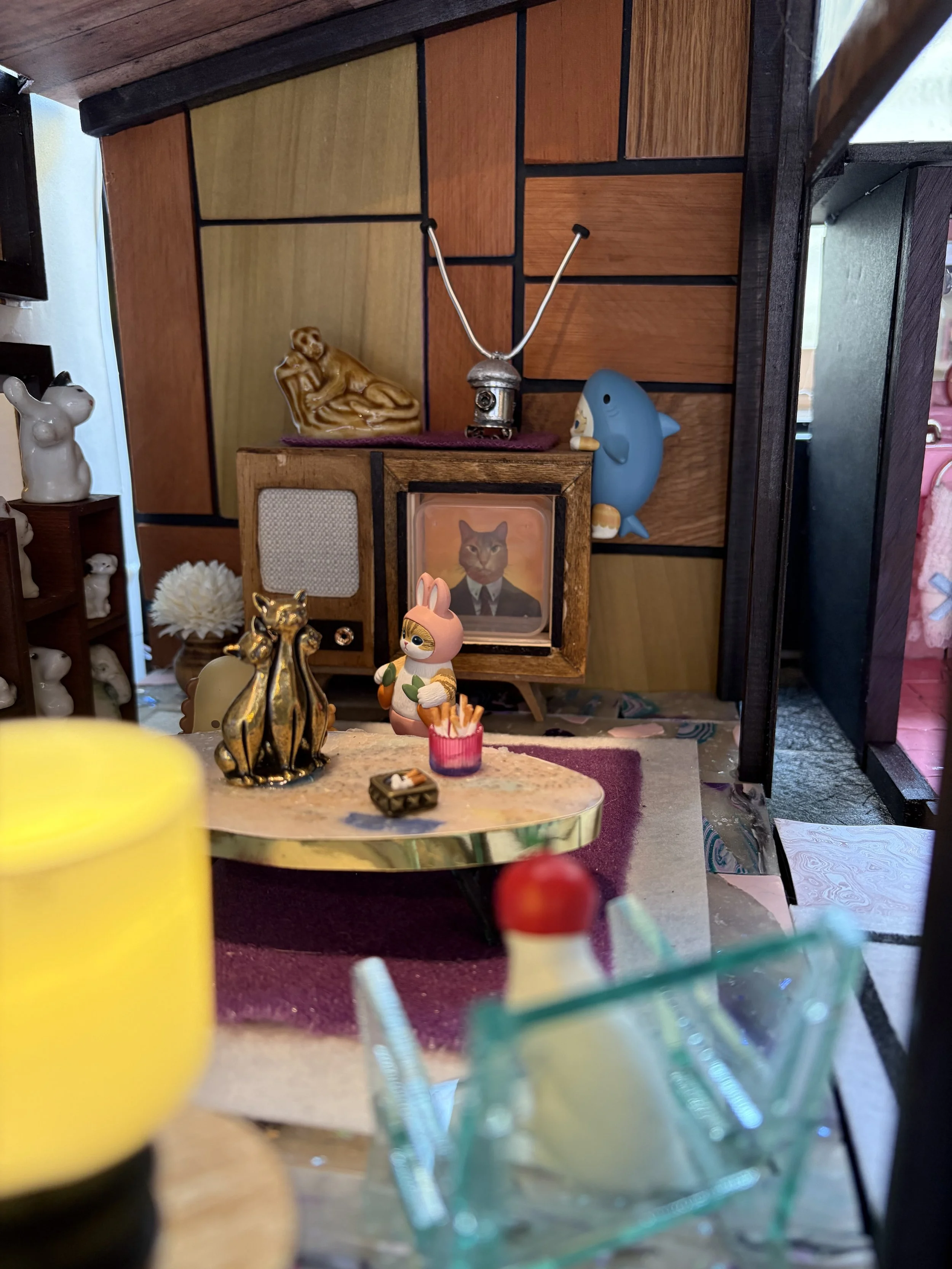 A display of various decorative items, including a ceramic bunny, a gold animal figurine, a small framed picture of a cat in a suit, a blue dolphin figurine, and a small pink bunny figurine on a marble table. In the background, there are wooden and d
