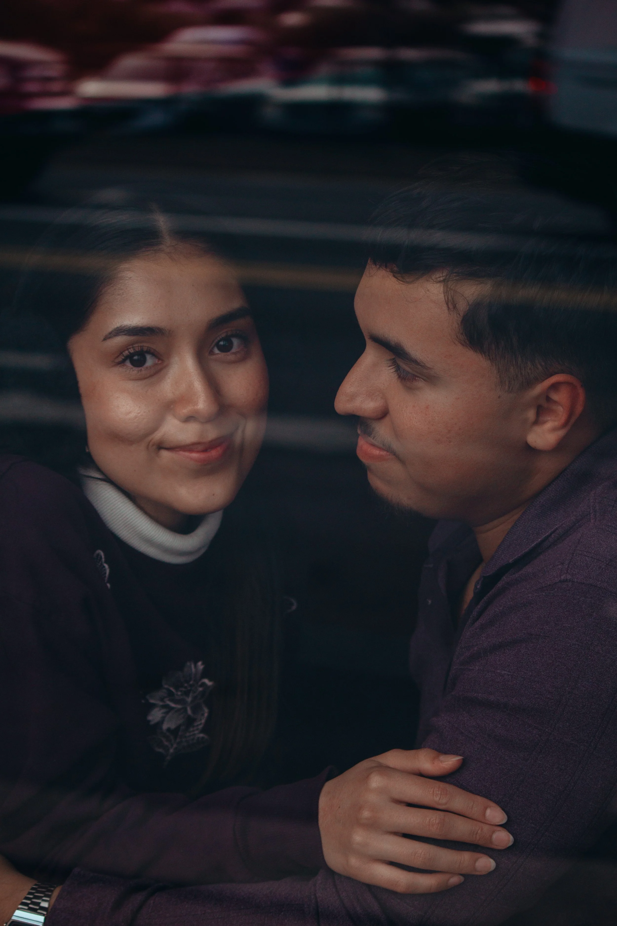 A woman with dark hair and a man with dark hair and a beard are lying underwater, facing each other and smiling.