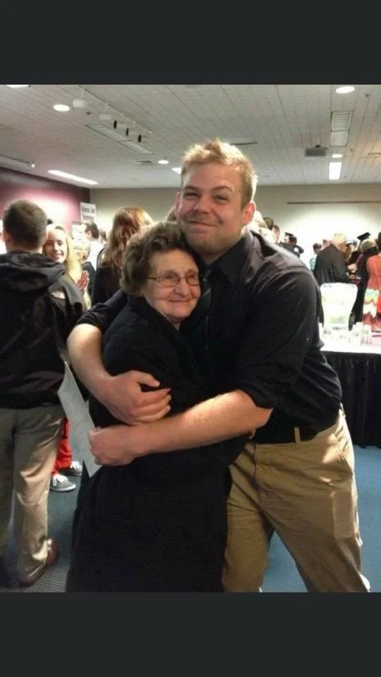 A young man hugging an older woman at a crowded indoor event.