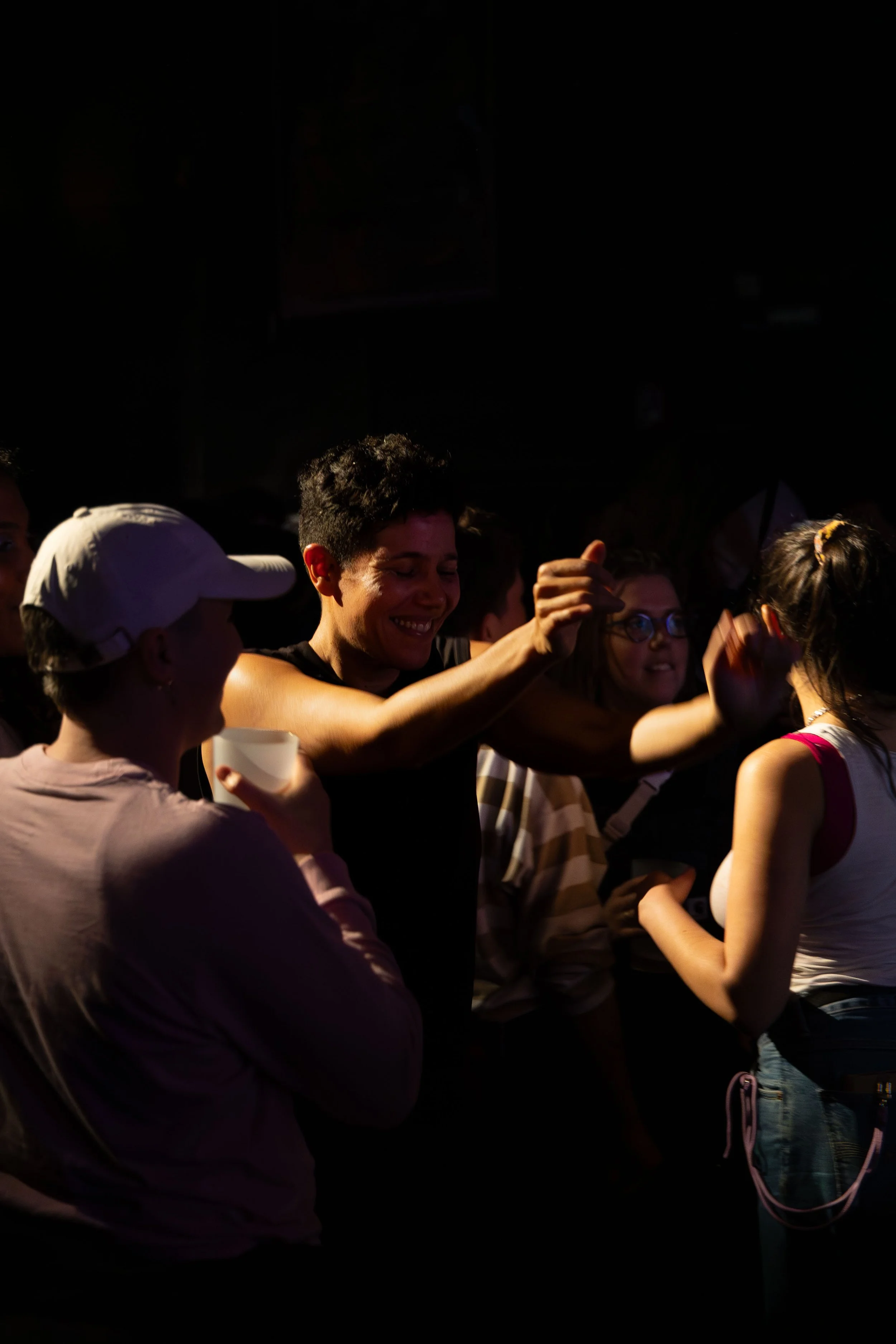 A group of people at an event, standing close together in a dimly lit environment, some smiling and interacting.