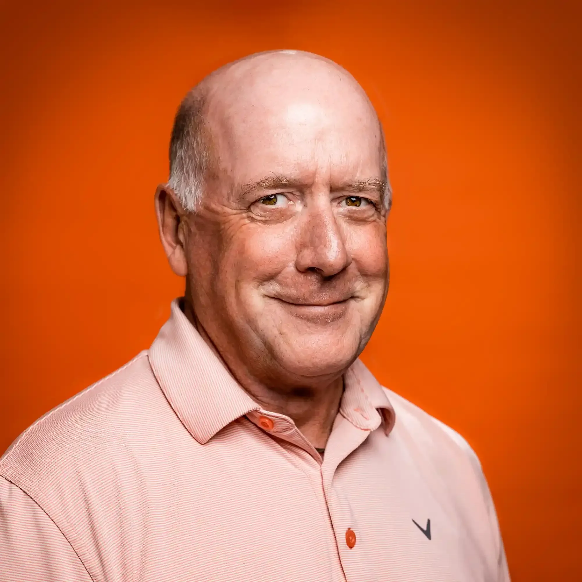 Portrait of a smiling middle-aged man in a light pink collared shirt against an orange background.