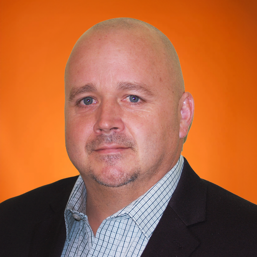 Headshot of a bald man with a light complexion, blue eyes, wearing a checkered shirt and a dark blazer, against an orange background.