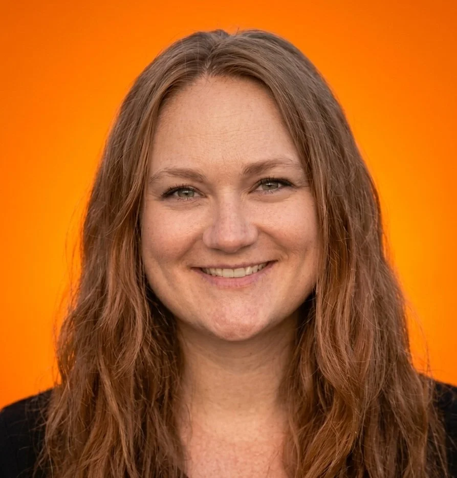 Close-up of a woman with long brown hair smiling against an orange background.