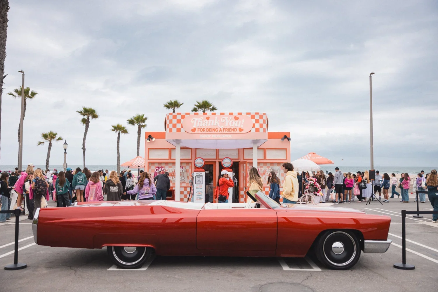 Classic red convertible car parked in front of a pink themed experiential brand activation booth and crowd near a beach - Evolve Activation