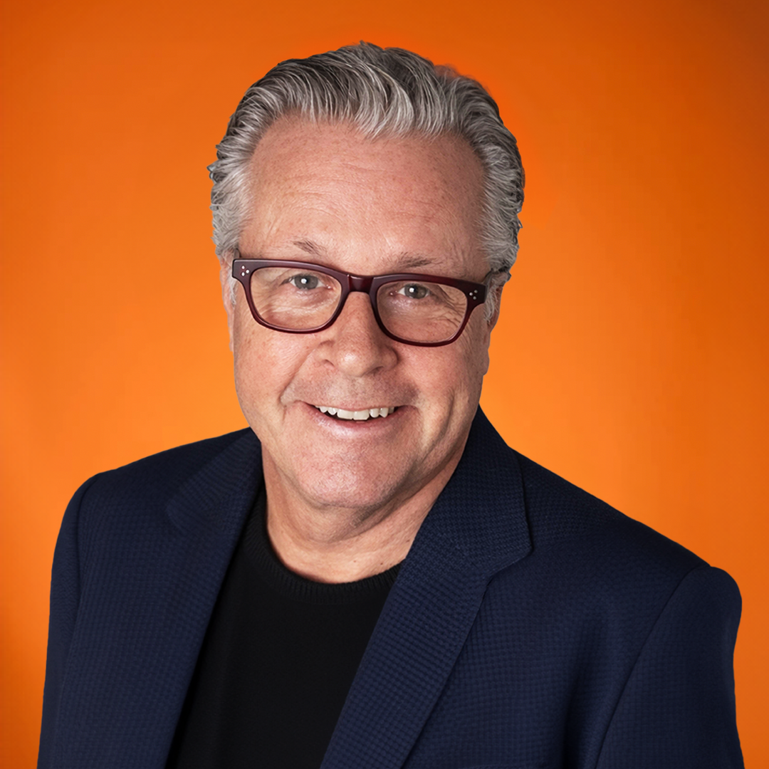 Portrait of a smiling middle-aged man with gray hair and glasses, wearing a dark blazer and black shirt against an orange background.