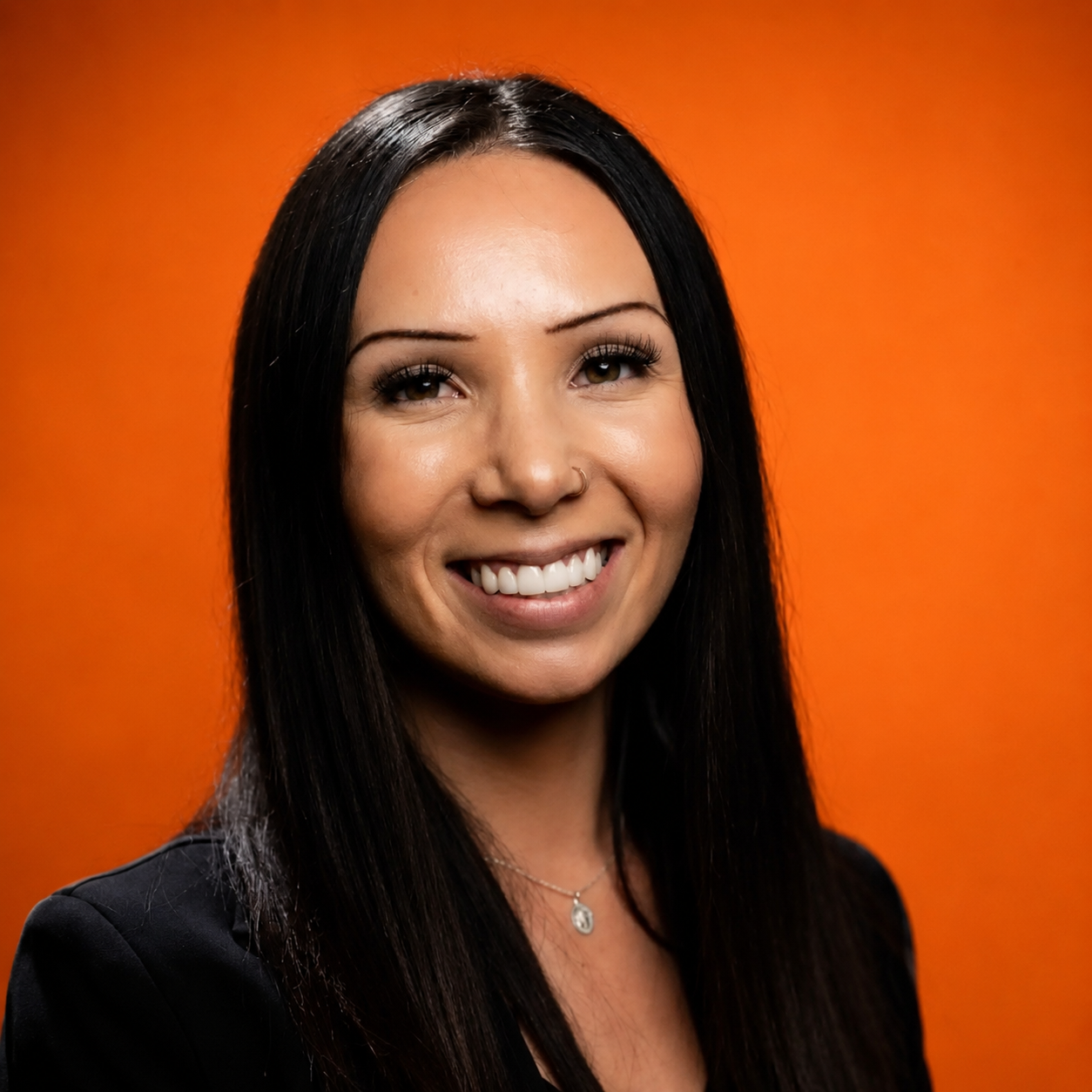 A woman with long dark hair smiling in front of an orange background.