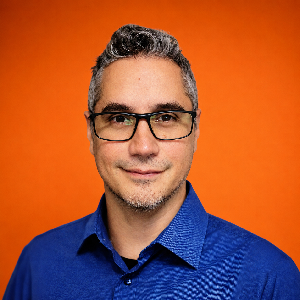 A smiling man with glasses and gray hair, wearing a blue shirt, against an orange background.