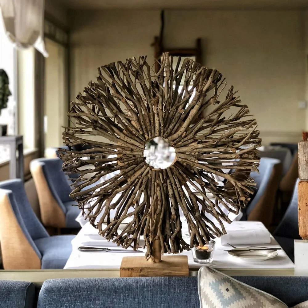 Decorative sculpture made from intertwined driftwood sticks arranged in a circular shape with a hole in the middle, displayed on a table in a dining room.
