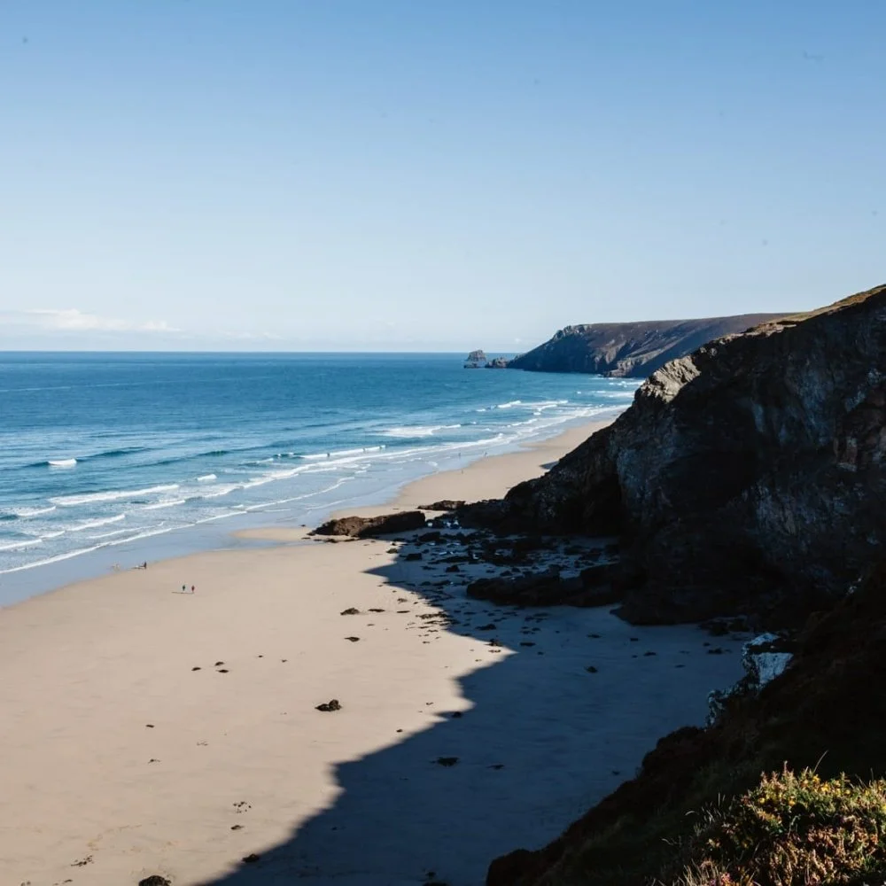A scenic beach with sandy shore, ocean waves, rocky cliffs, and clear blue sky