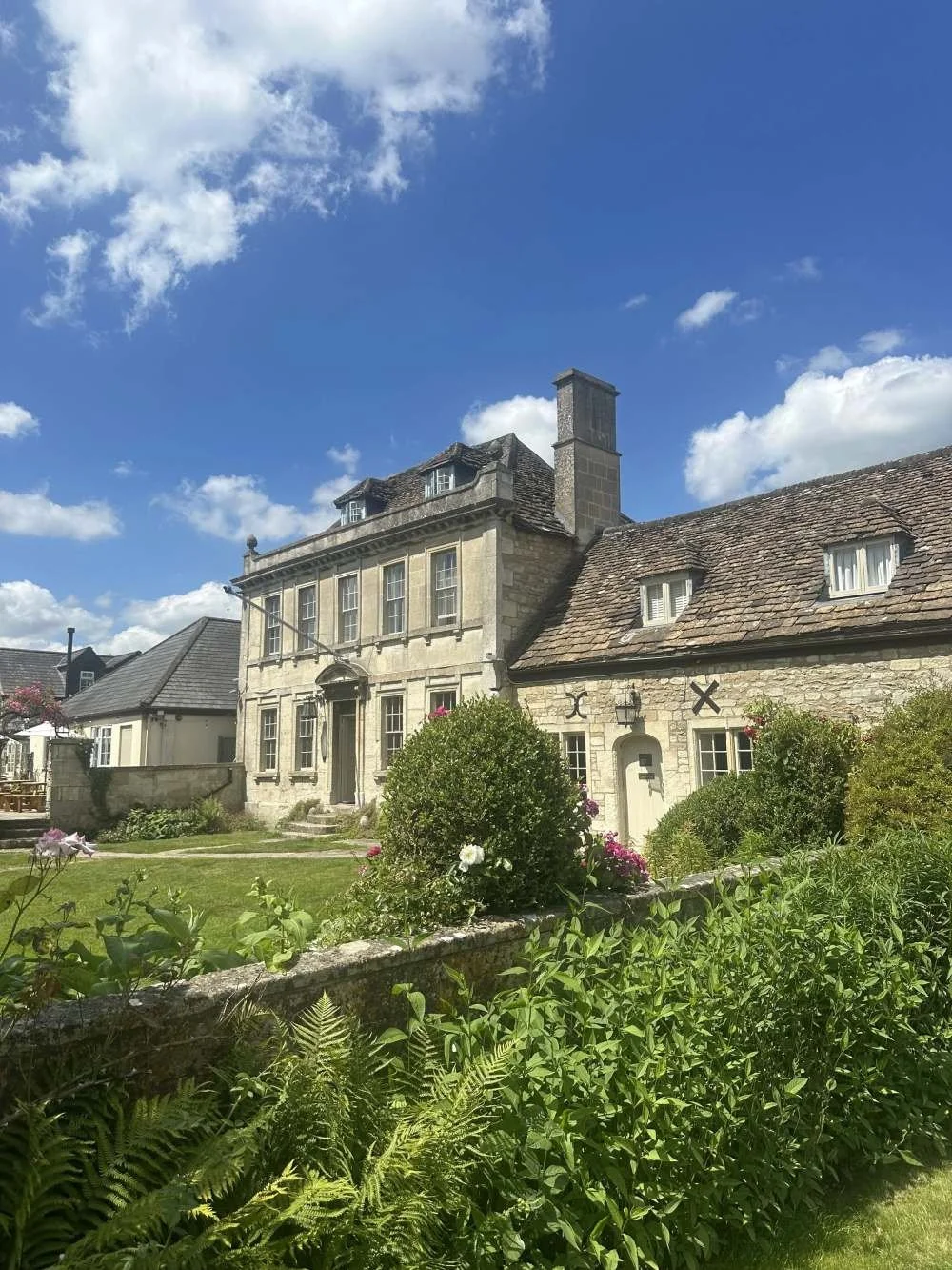 A historic stone house with a landscaped garden under a blue sky with white clouds.
