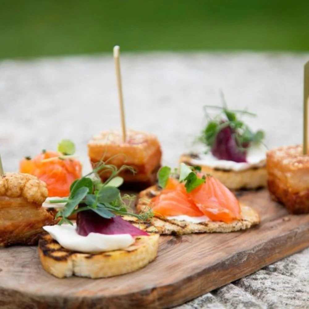 Assorted small appetizers on a wooden serving board, including smoked salmon on toast, grilled bread with toppings, and various garnishes.