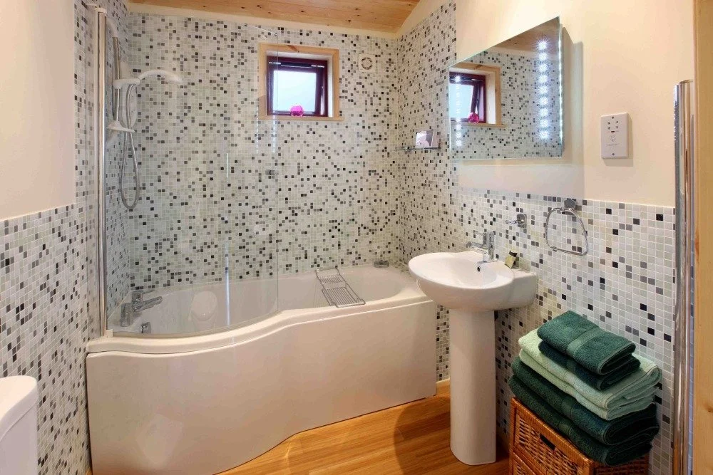 Bathroom with a bathtub, a small window, a pedestal sink, a mirror, and neatly folded towels on a wicker basket.