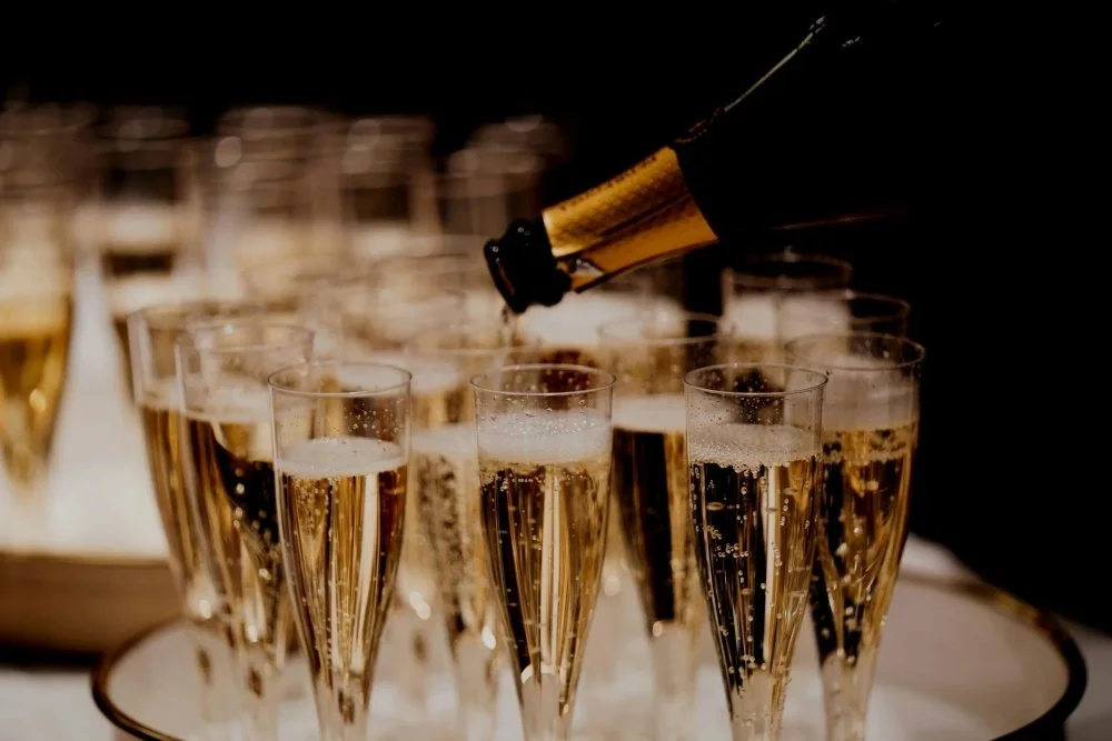 Champagne flute glasses being filled with bubbly champagne from a bottle at a celebration or party.