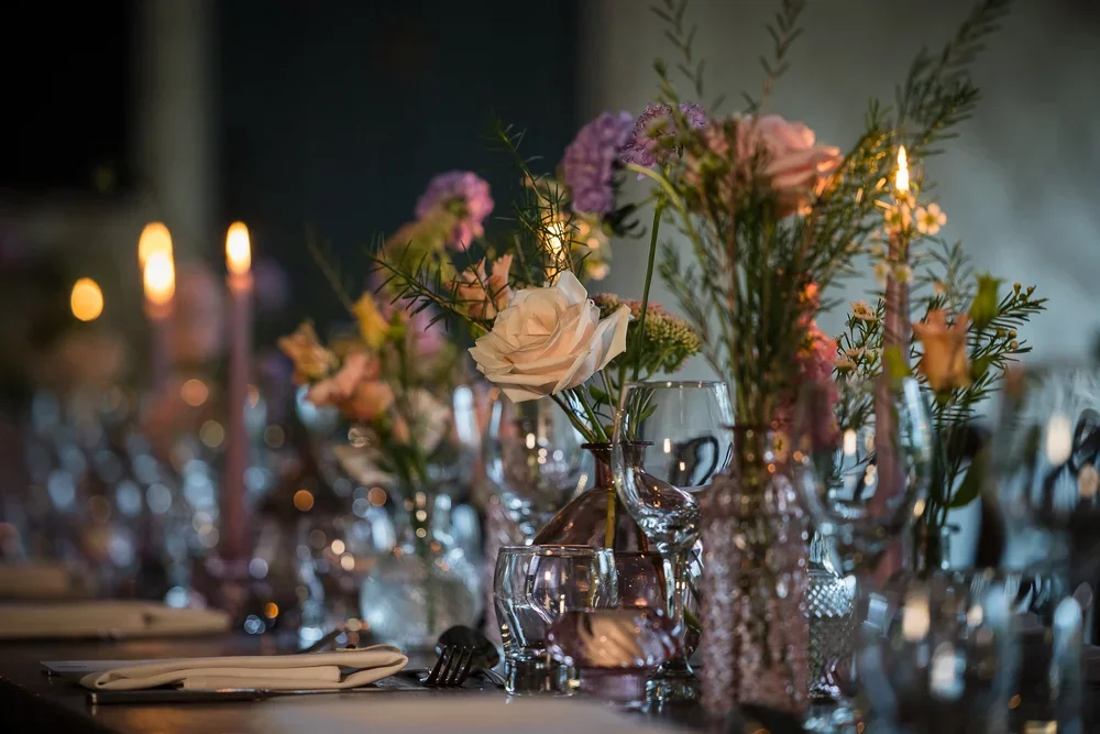 Elegant table setting with floral centerpieces, candles, wine glasses, and silverware.