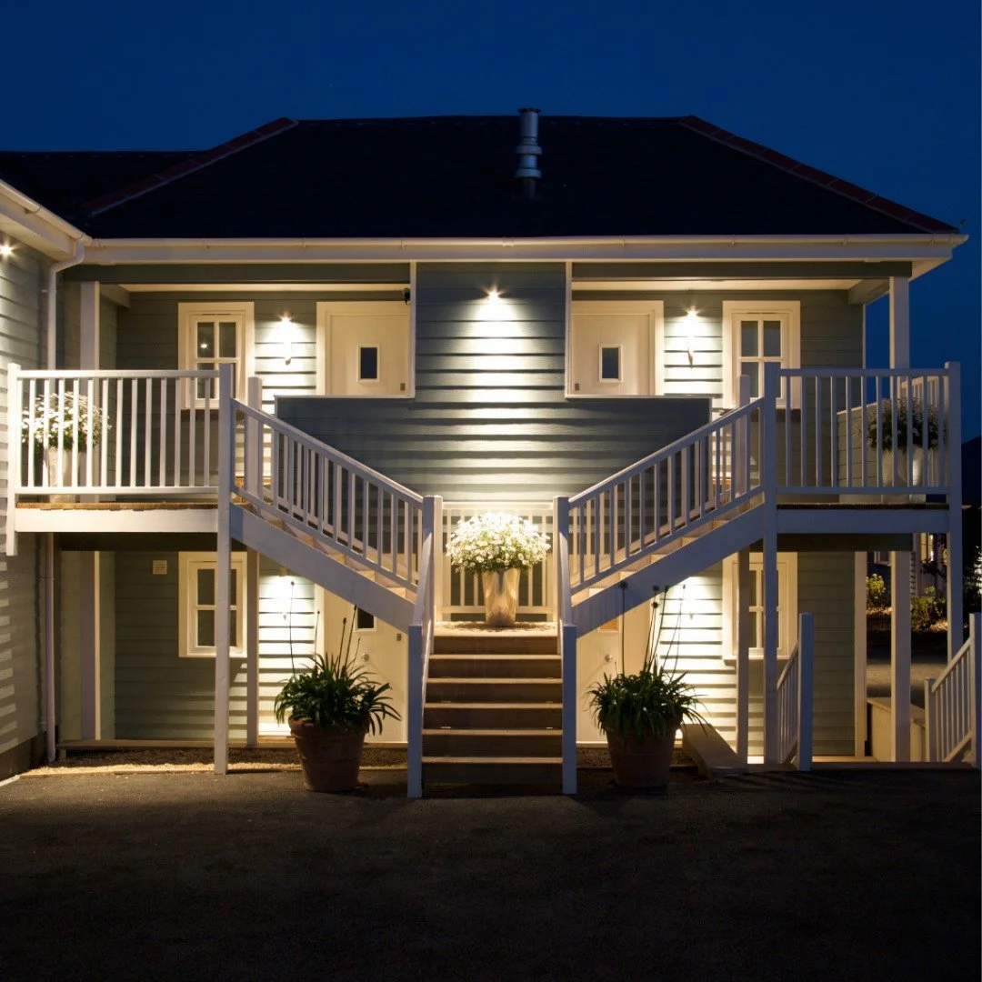 Illuminated two-story house at night with a central staircase, flower pots, and white railings.