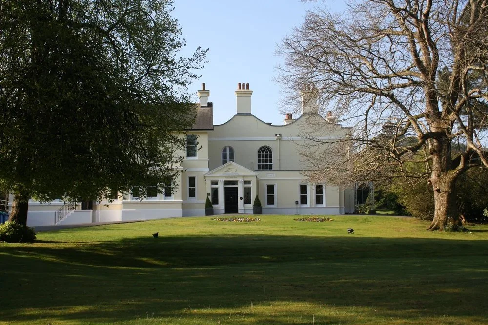 A large, white, historic house with a manicured lawn and trees in front.