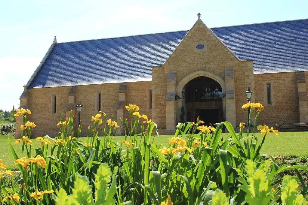 Yellow flowers in front of a stone church with a blue roof and cloudy sky.