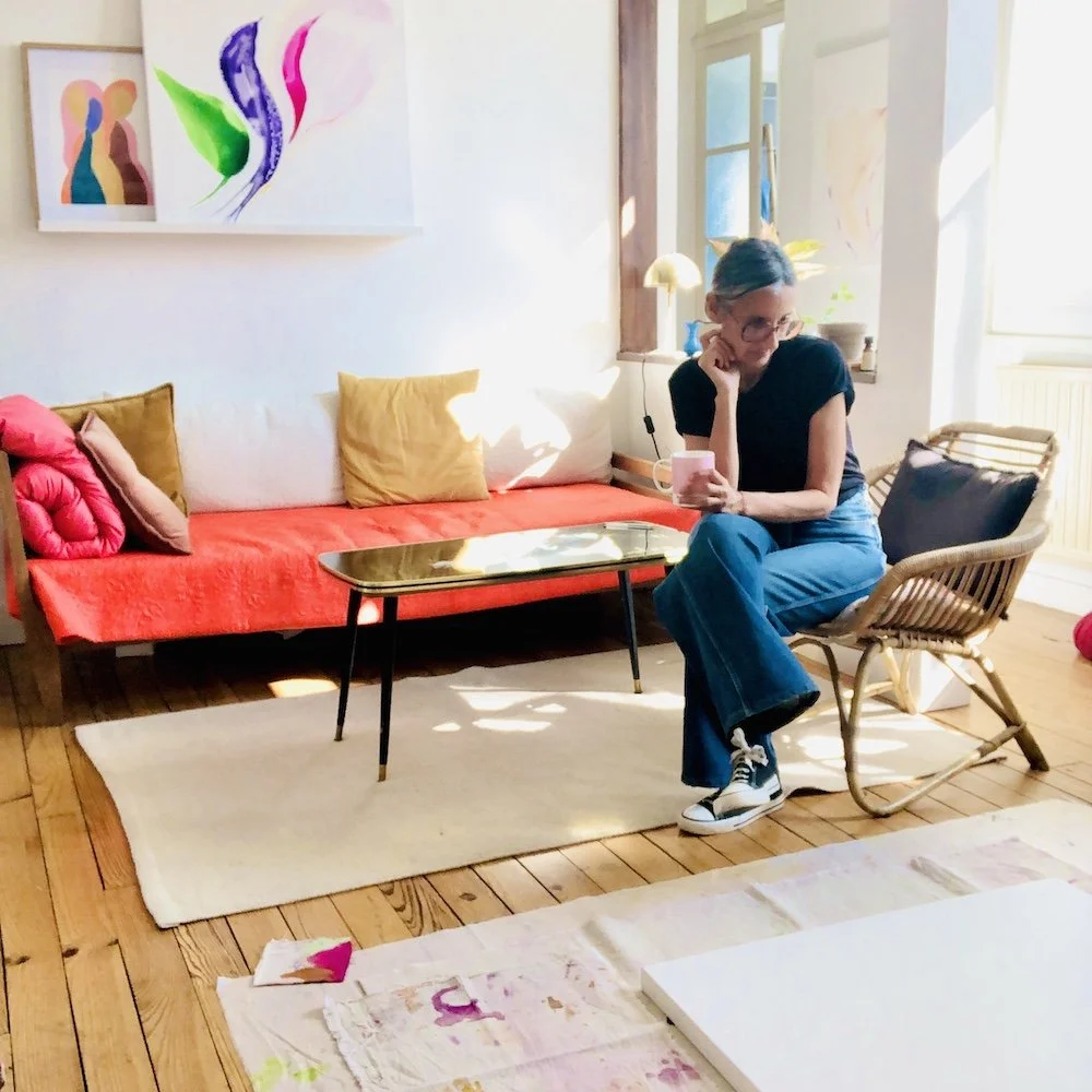 Portrait de l’artiste dans son intérieur, entourée de toiles intuitives et de couleurs vibrantes.