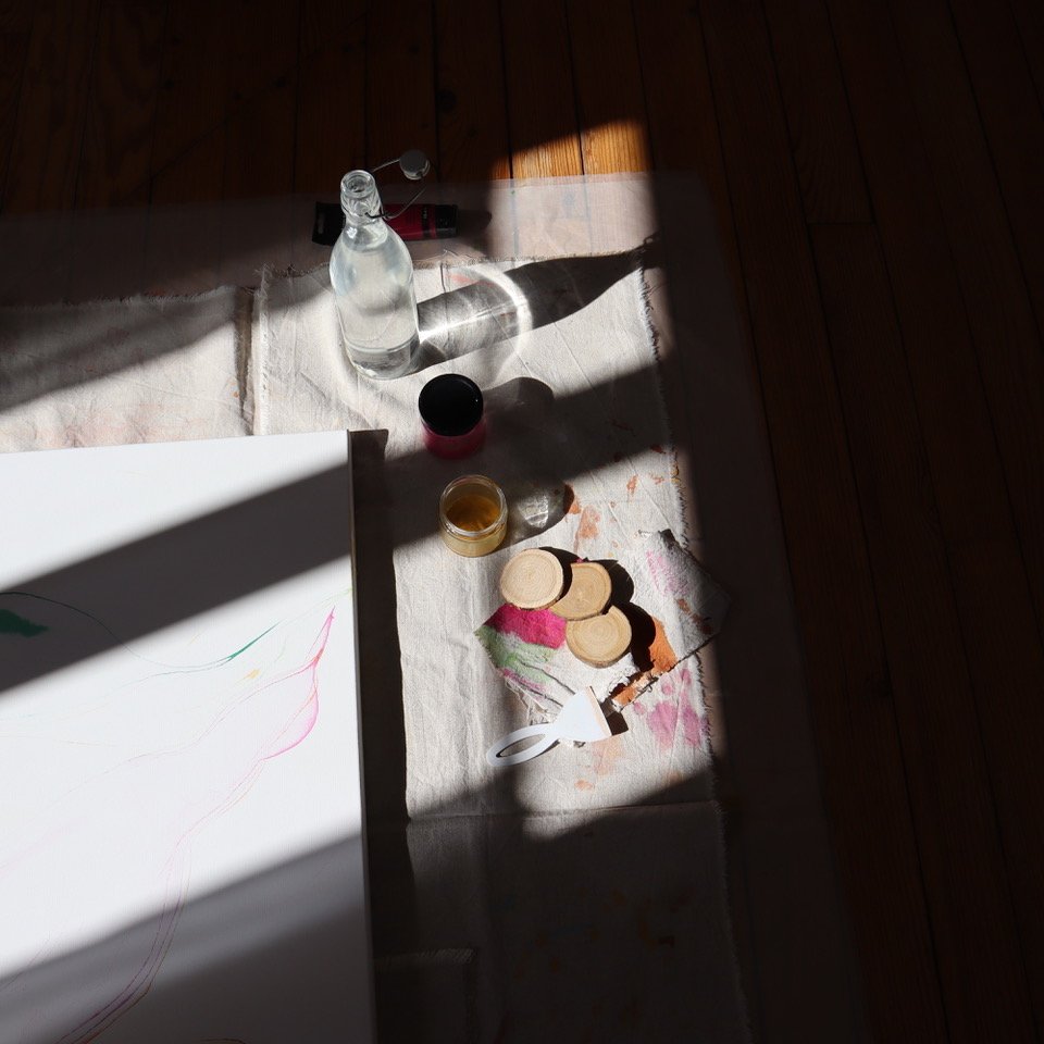 Toile et peinture en cours, posée au sol dans un rayon de soleil.