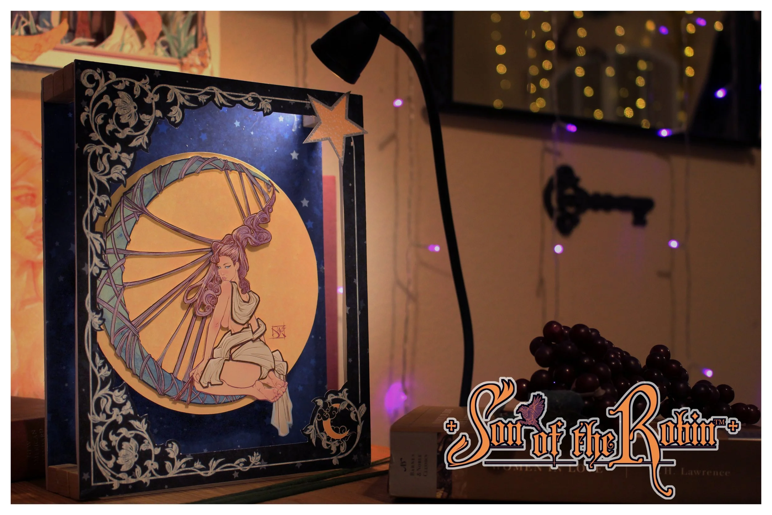 "Lunar Entanglement", a 3D Storybox by artist Anthony Christopher Robinson, featuring a vintage-style woman draped in white sitting in the crescent moon in the sky. The background has string lights creating a cozy atmosphere.