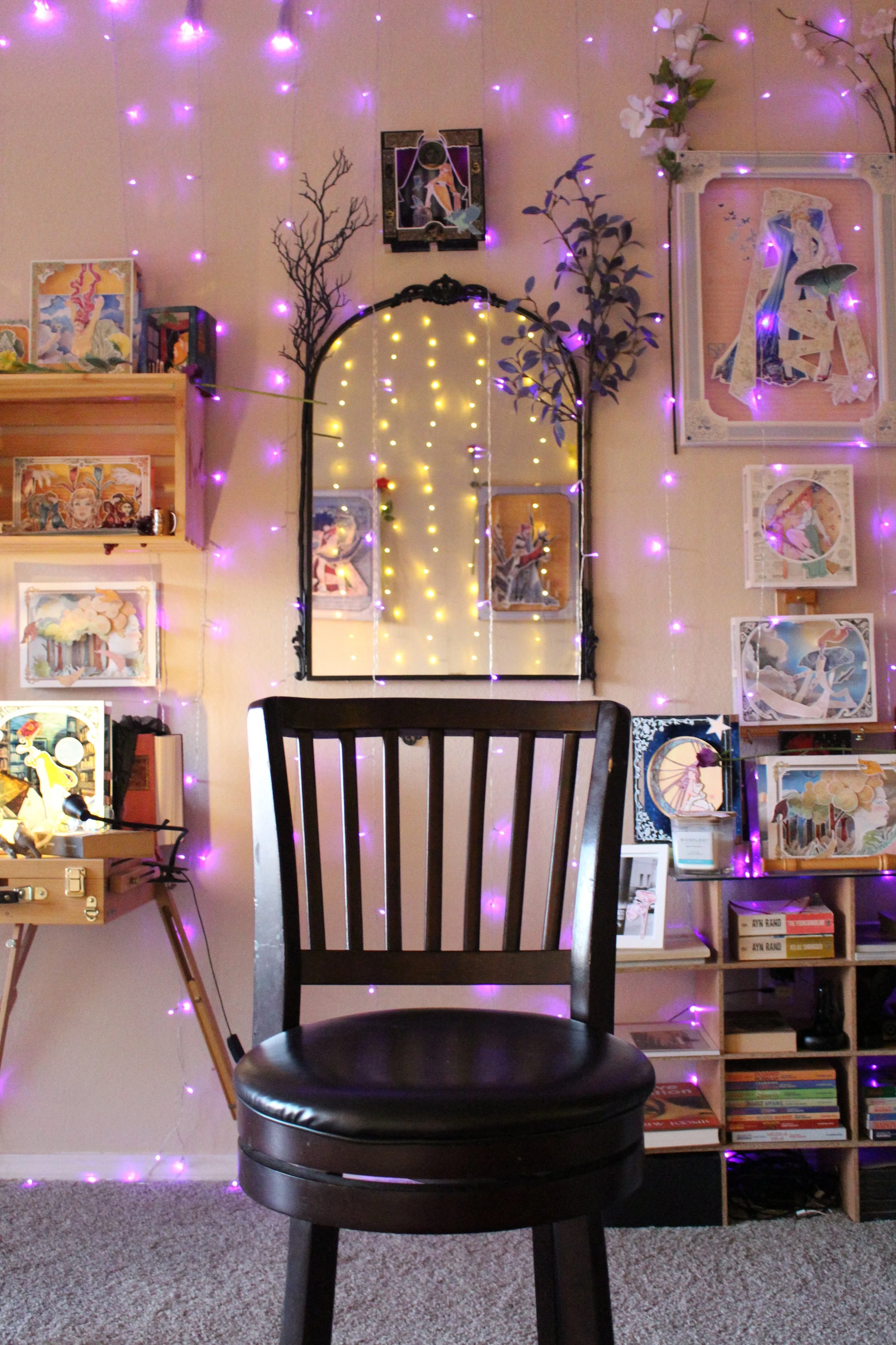 A cozy room decorated with wall art, fairy lights, a mirror, a small bookshelf, and a wooden chair in the foreground.