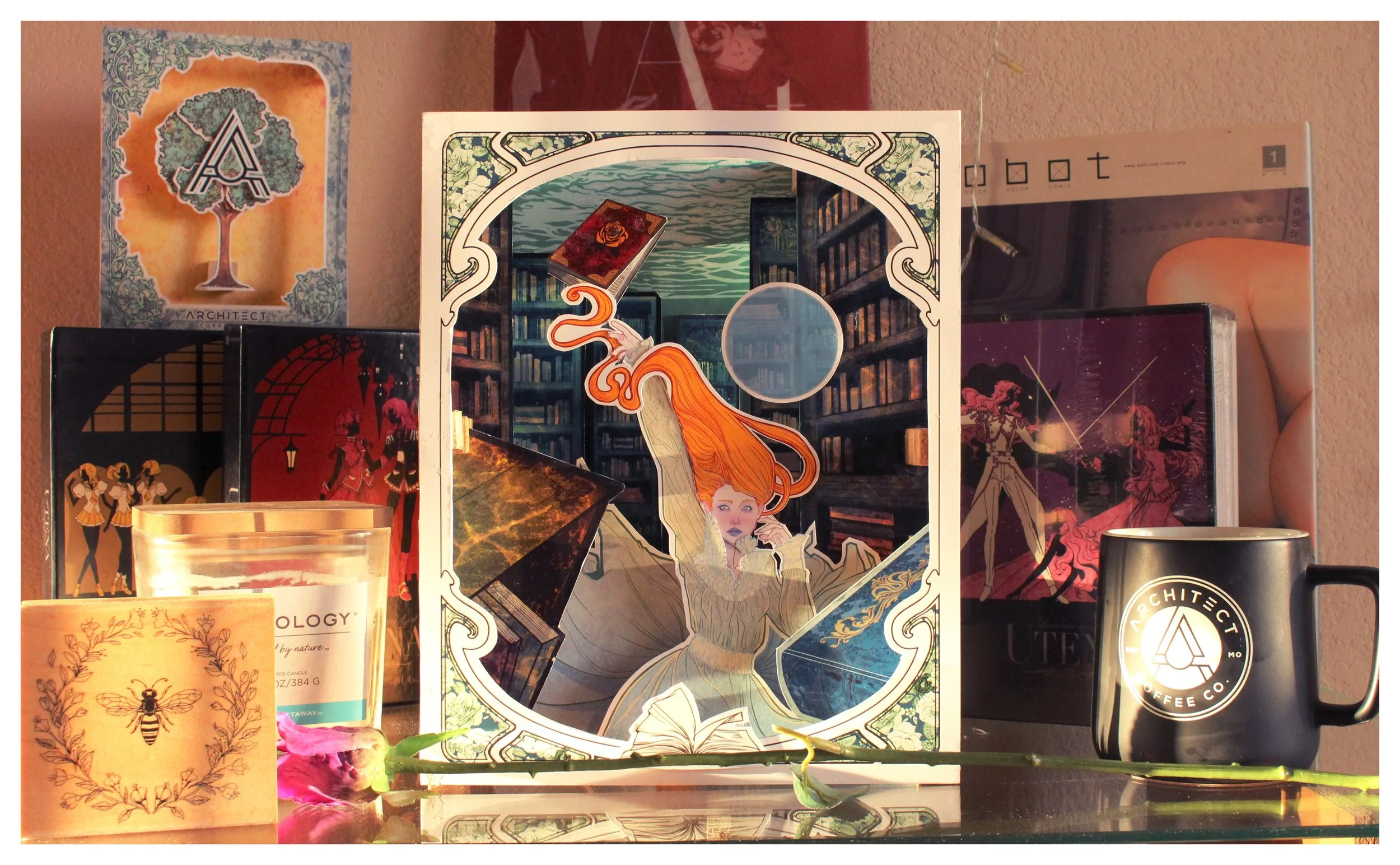 A collection of various items including a card with an illustration of a young woman with orange hair and a library background, books, a candle with a bee illustration, and a coffee mug on a shelf.