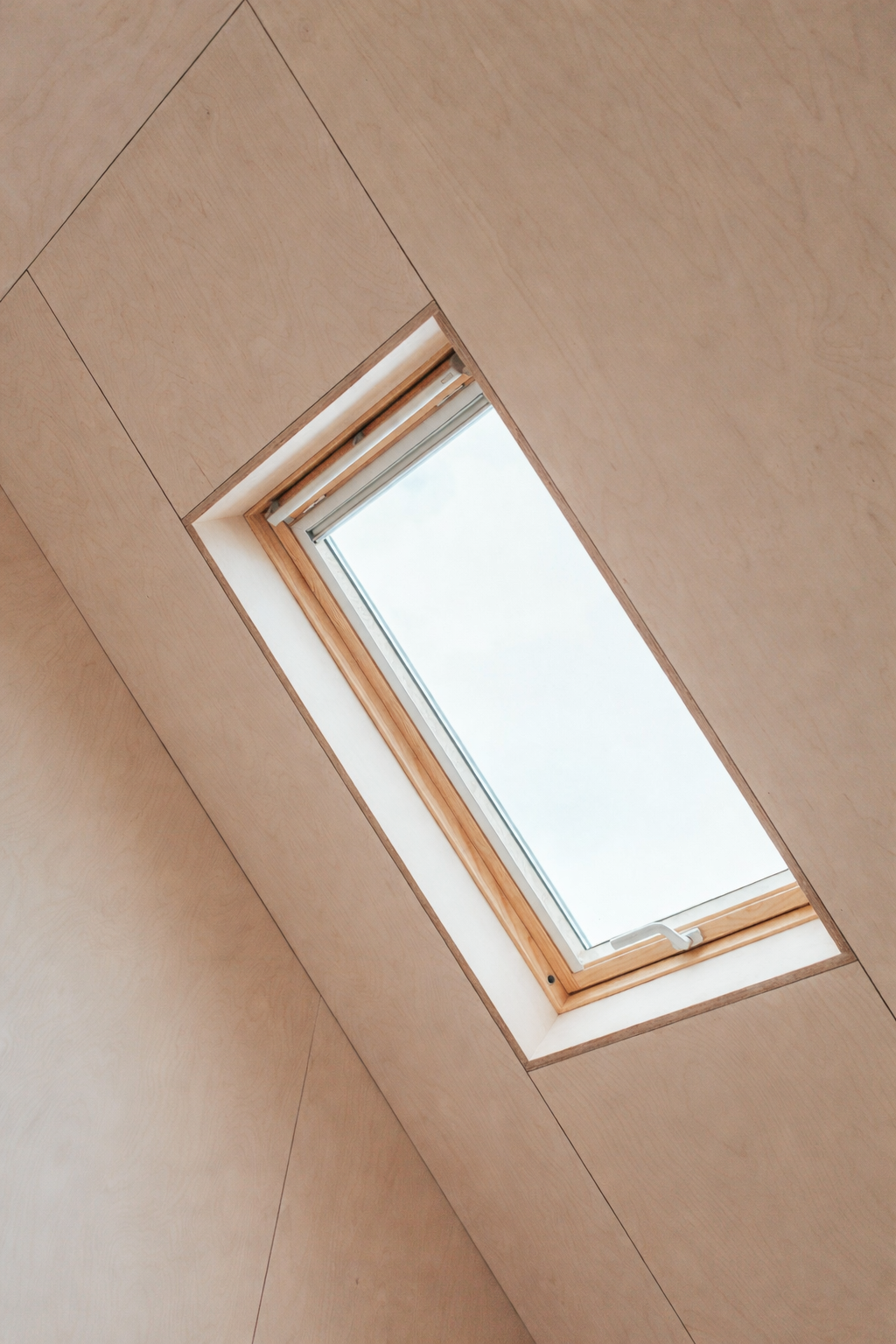 Ein Dachfenster in einer Holzwand im Innenraum, zeigt den Himmel außerhalb.