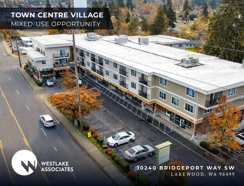 Aerial view of a mixed-use commercial and residential building on a city street in Lakewood, Washington, with parked cars, trees with autumn foliage, and a sign for Westlake Associates.