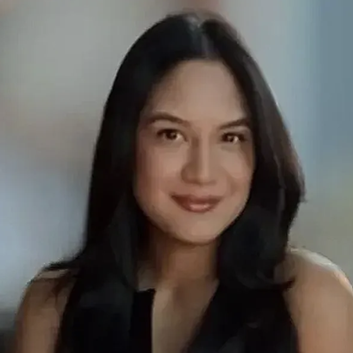 A woman with long, dark hair and makeup, wearing a sleeveless black top, smiling at the camera.