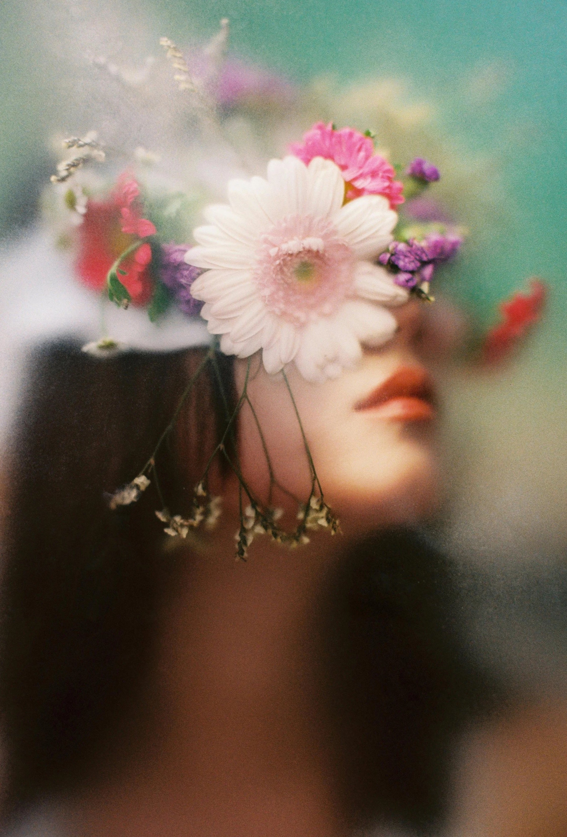 A woman with dark hair and lipstick holds a bouquet of various colorful flowers, partially covering her face.