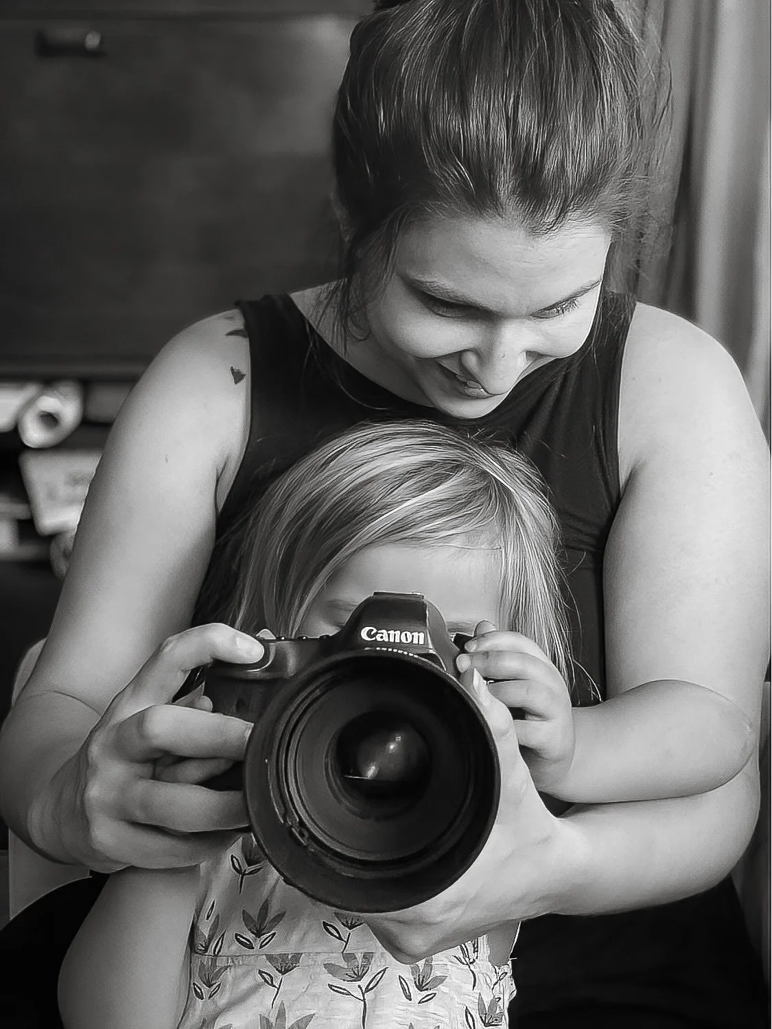 A woman and young girl taking a selfie with a Canon camera, smiling and holding the camera together.
