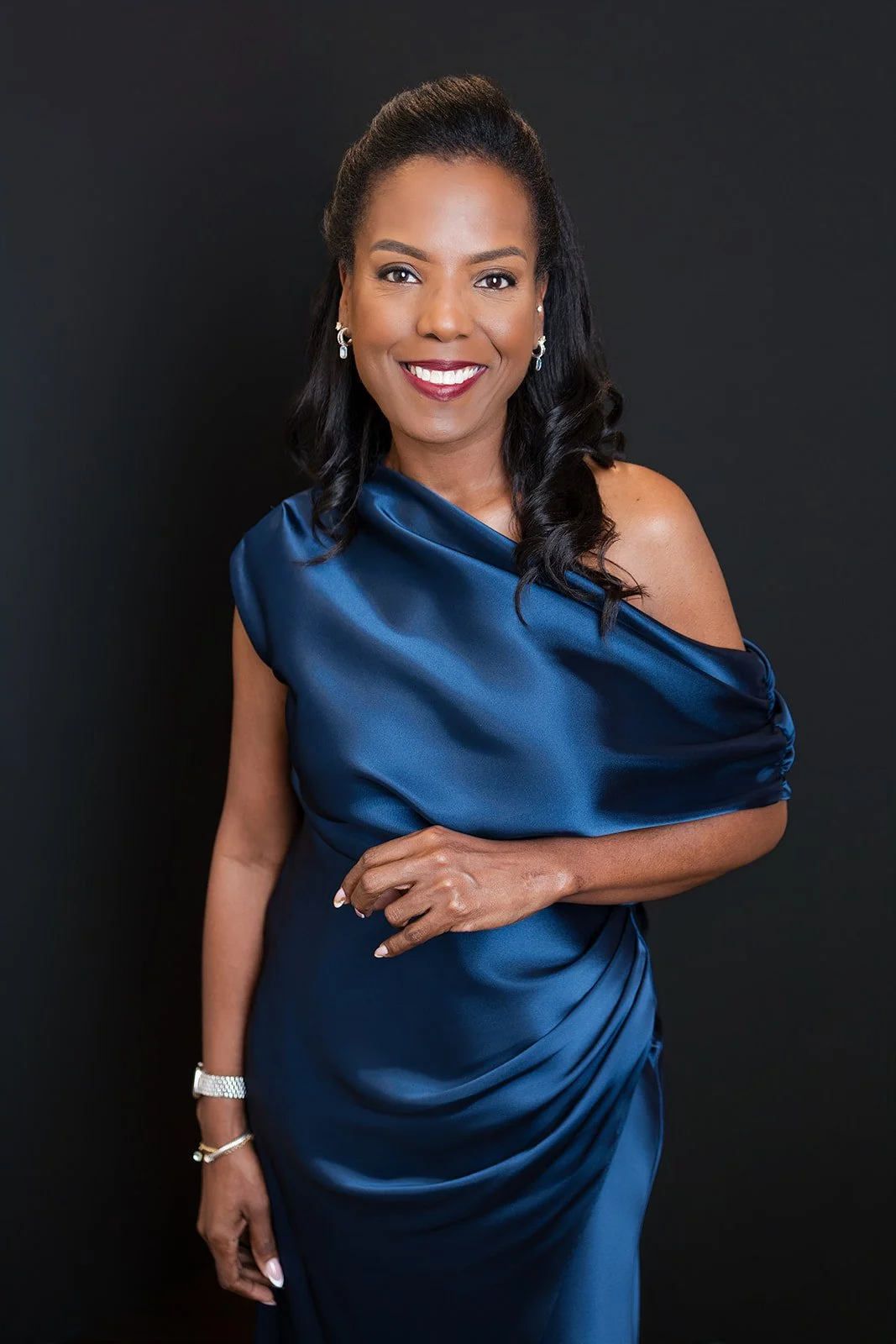 Portrait of an African American woman smiling, dressed in a royal blue satin gown, against a black background.