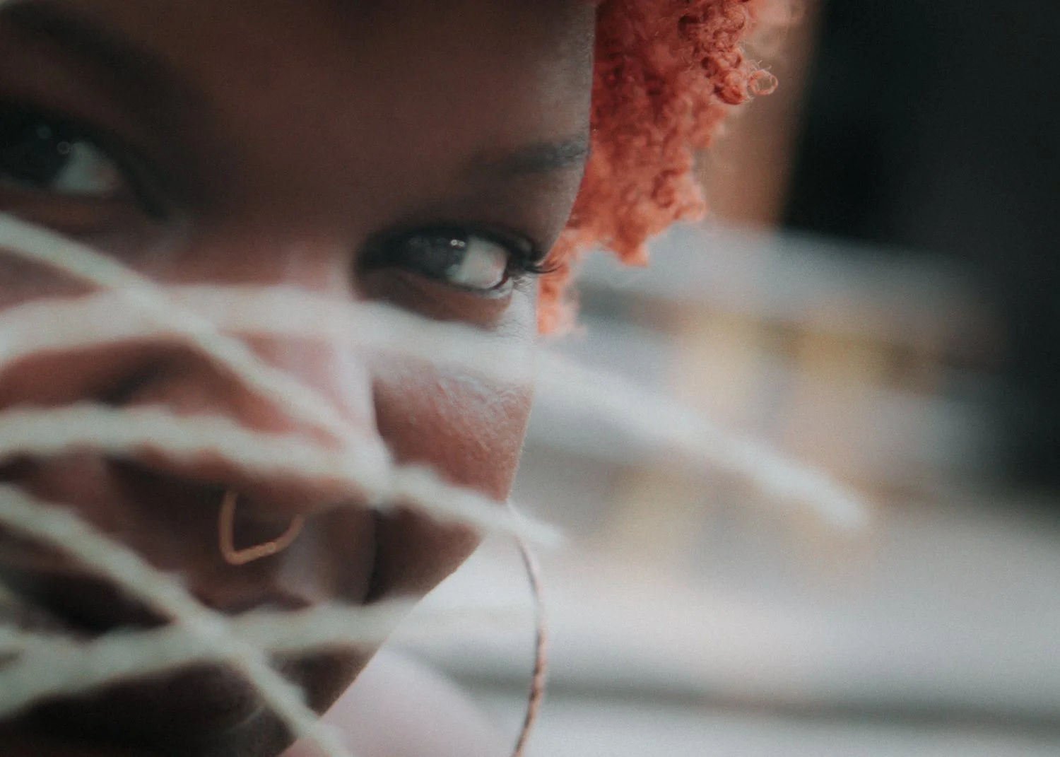 Close-up of a person with orange braids looking downward, with glasses on, resting their head on their hand.