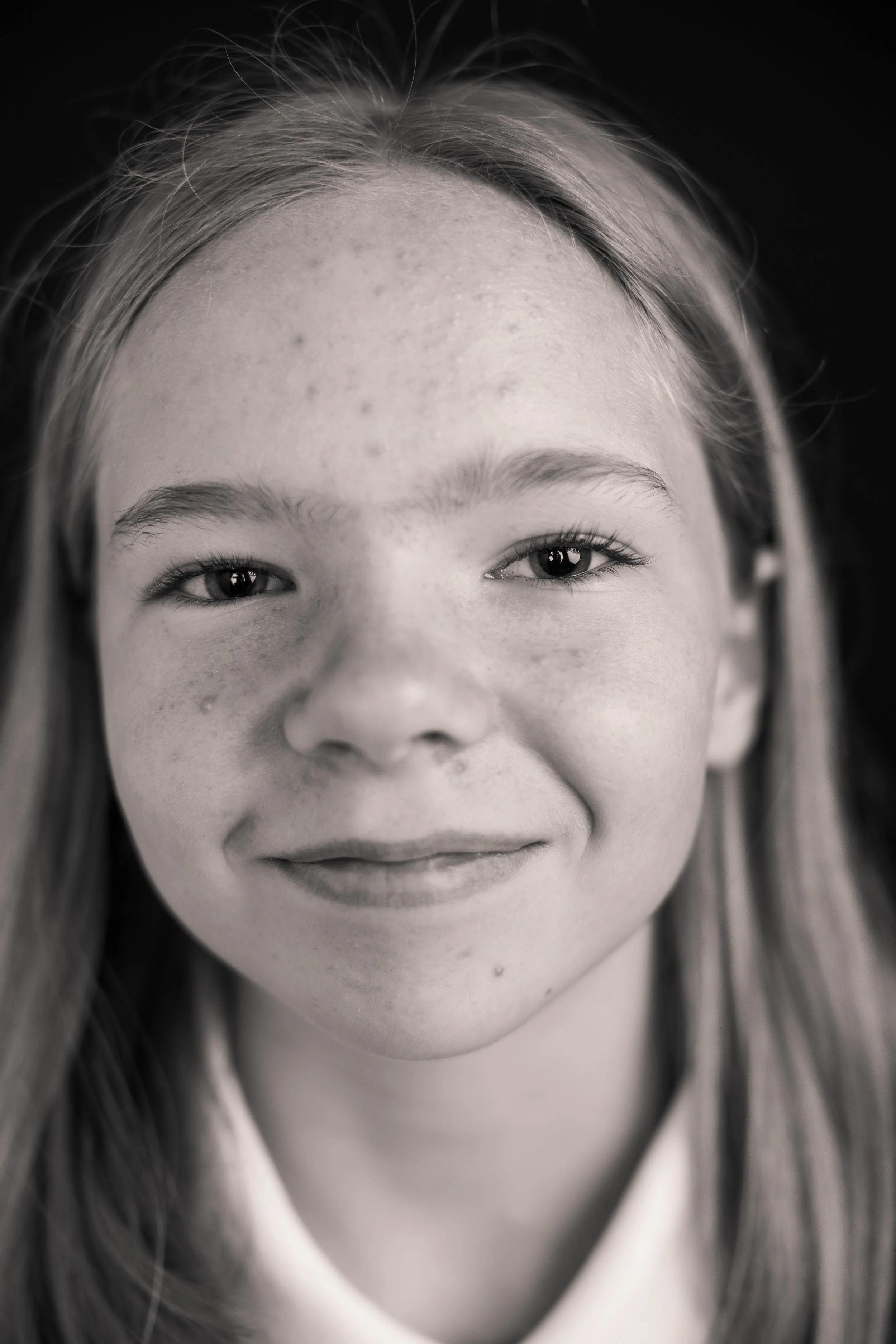 Close-up black-and-white photo of a young girl's face, focusing on her eyes, forehead, and part of her mouth, with long hair and a gentle smile.