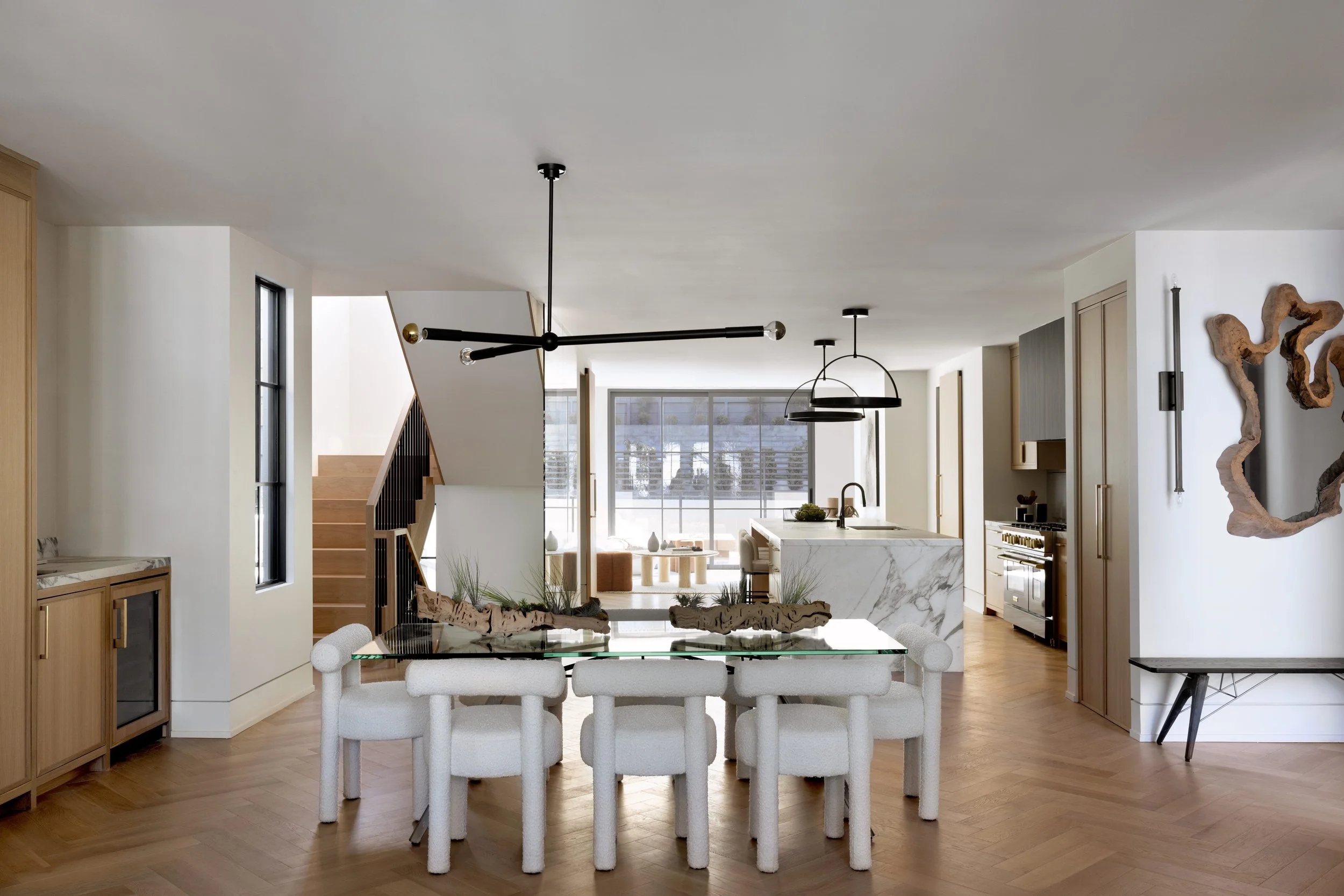Open-concept middle room with modern dining table, white chairs, kitchen with marble island, and decorative wall art.