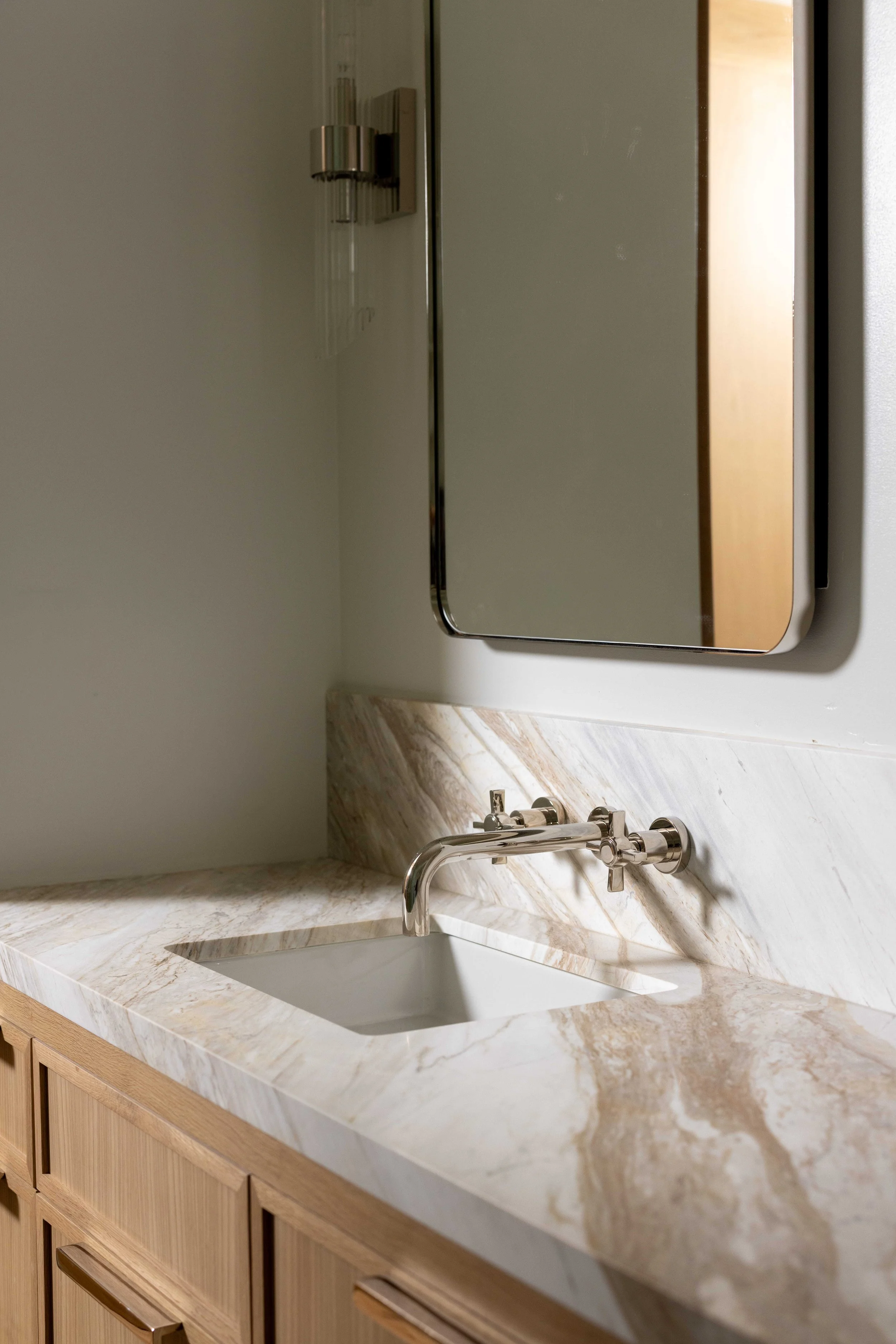 Bathroom vanity with marble countertop, under-mount sink, wall-mounted faucet, mirror, and wooden cabinet.