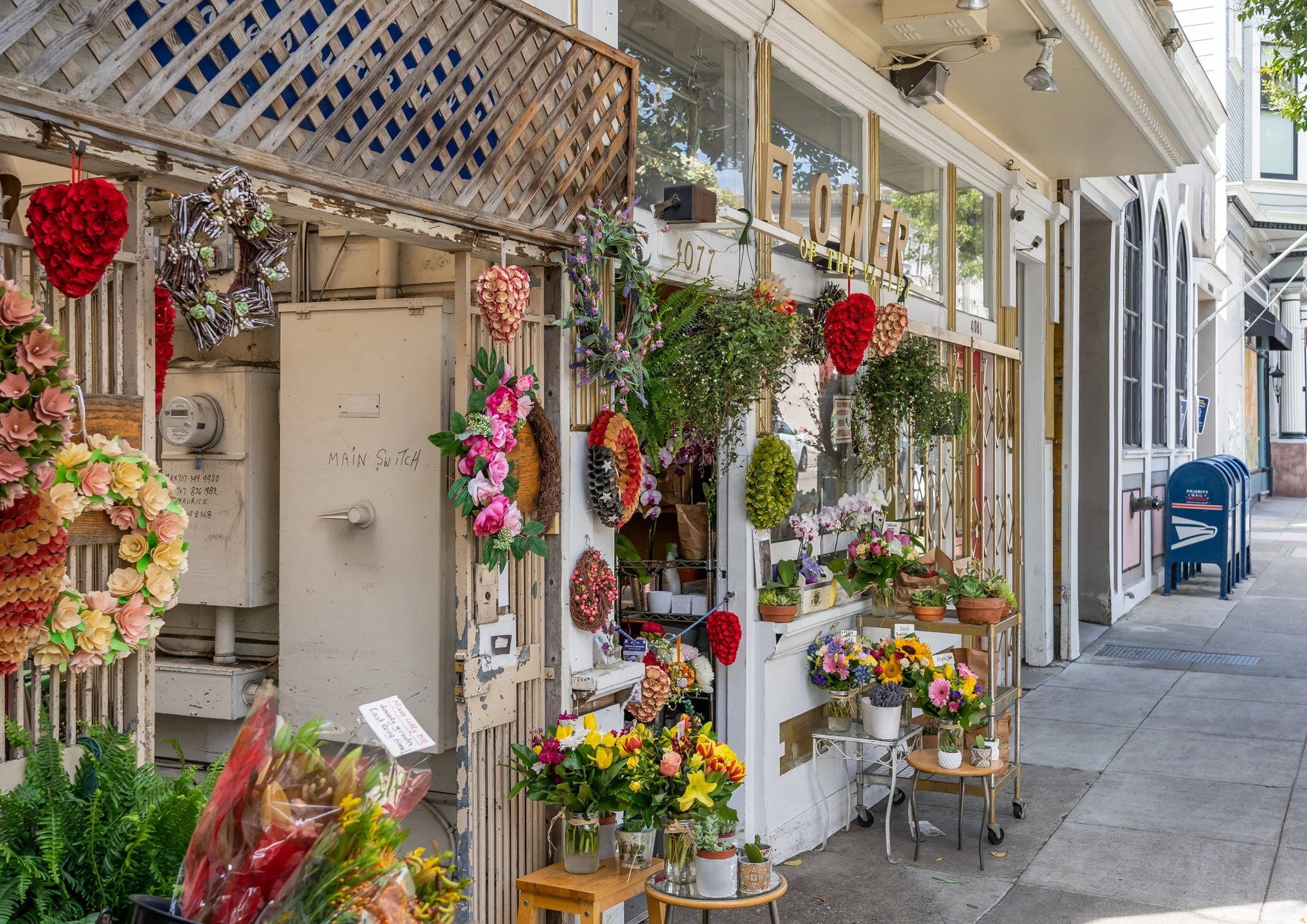 Flower shop storefront decorated with colorful wreaths and potted flowers on sidewalk in urban area.