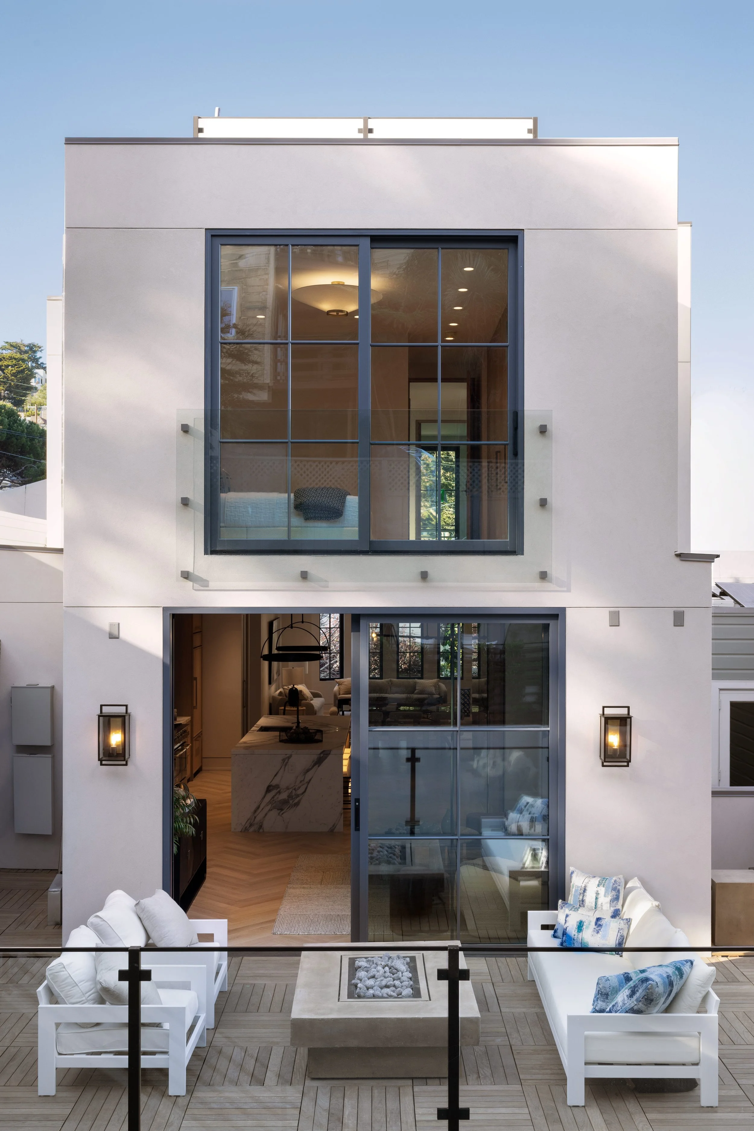Modern two-story house with outdoor patio, white seating, fire pit, and large glass windows