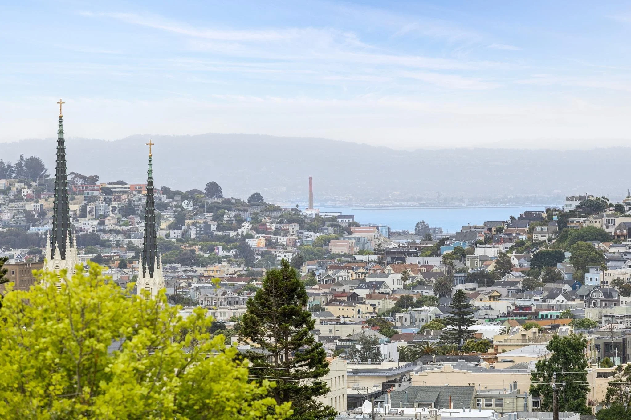 A cityscape view of San Francisco with the Transamerica Pyramid and Golden Gate Bridge in the background, seen through a light haze on a cloudy day, with residential and commercial buildings in the foreground.