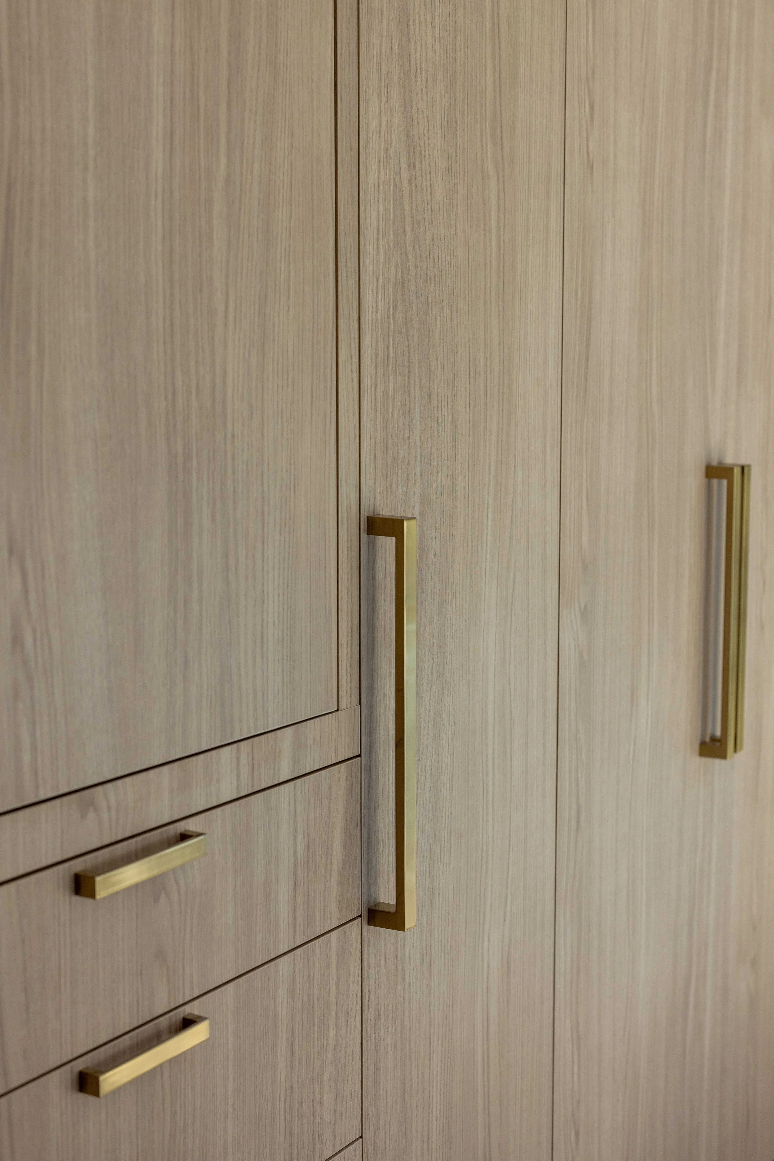 Close-up of a wooden cabinet with vertical wood grain and gold bar handles.