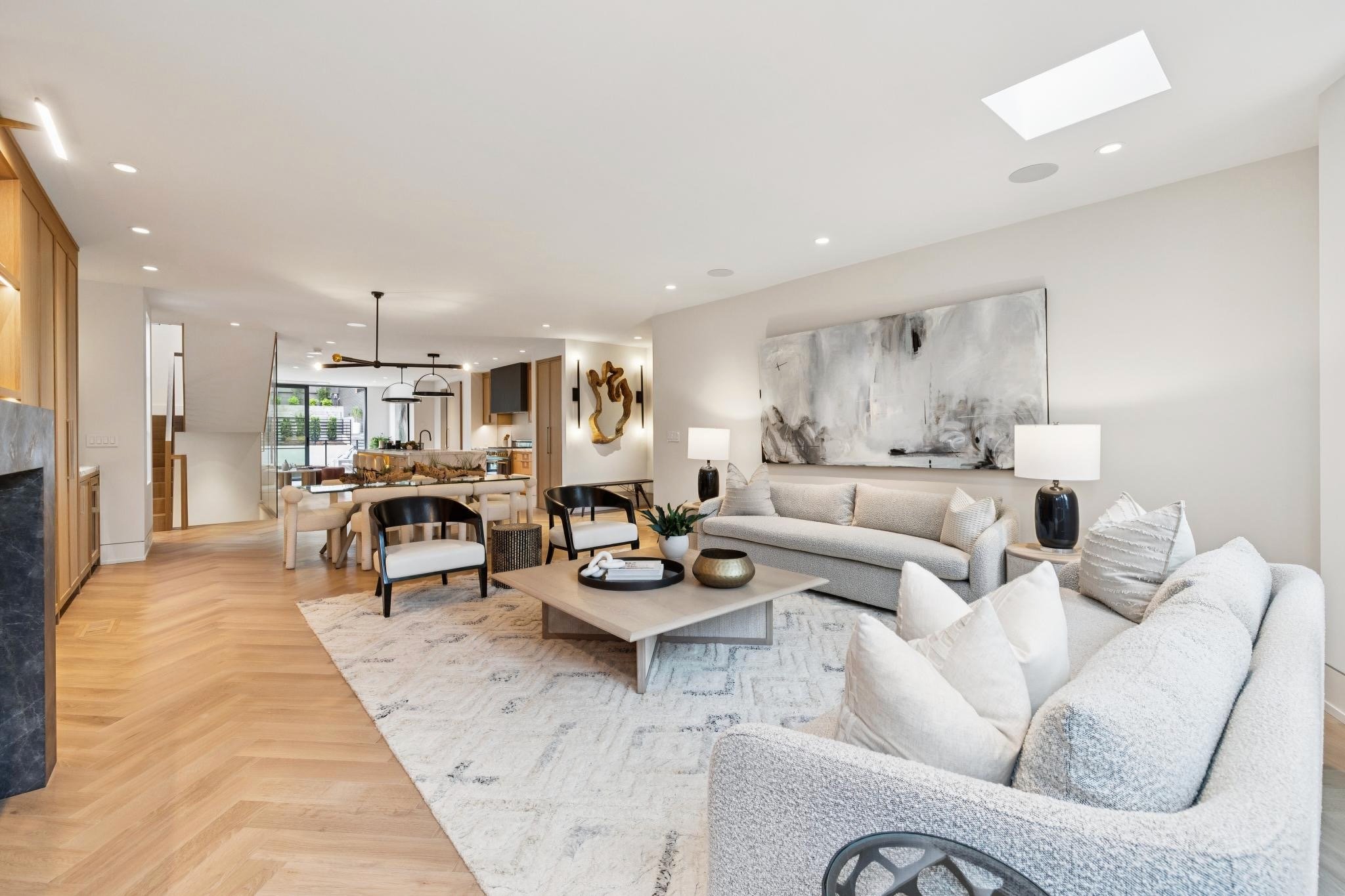 Open-concept living room and dining area with modern furniture, abstract wall art, and hardwood flooring.