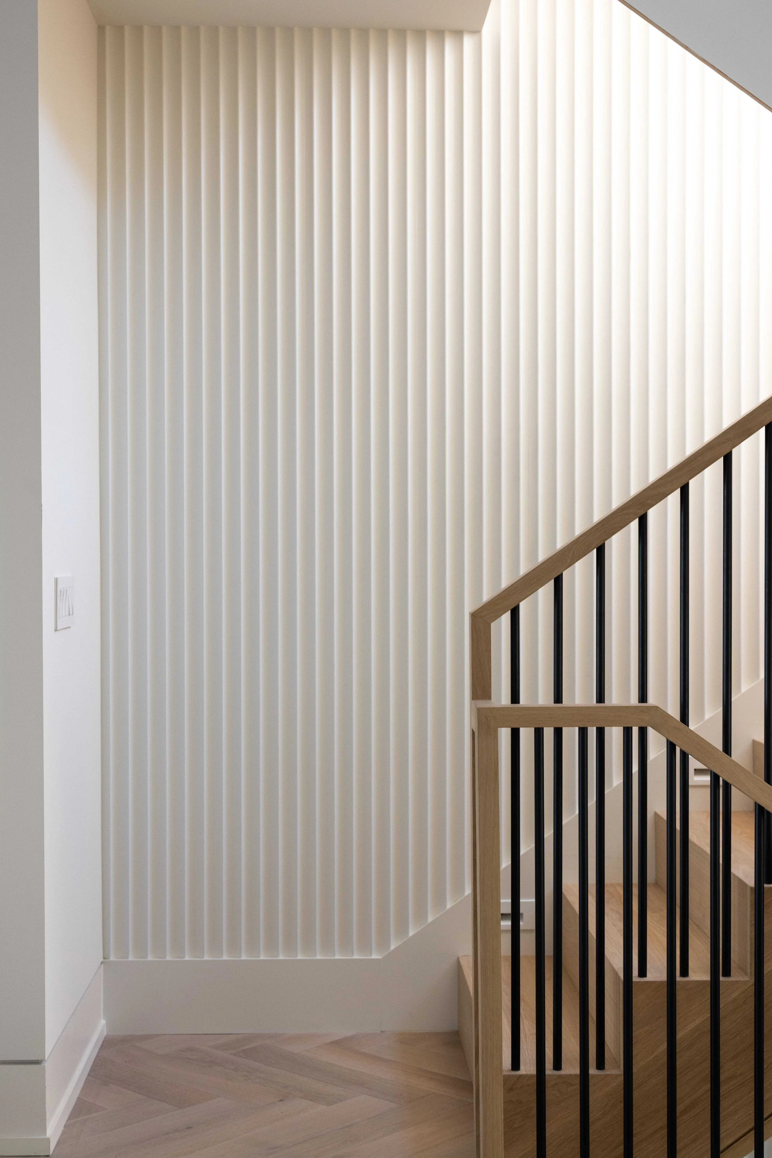 Interior view of a staircase next to a textured wall with vertical, evenly spaced ridges in a modern home.
