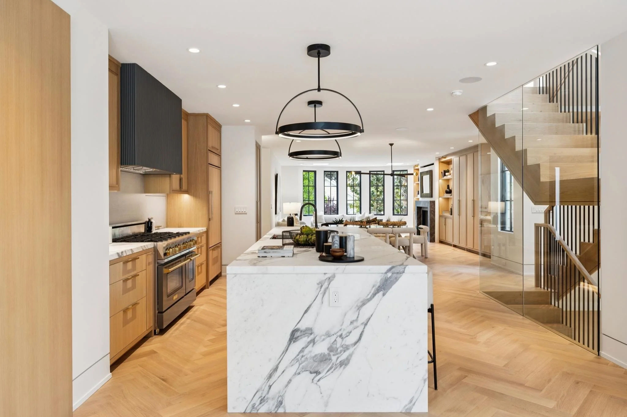 Open-concept kitchen with a marble island, wooden cabinets, black appliances, and modern lighting fixtures.