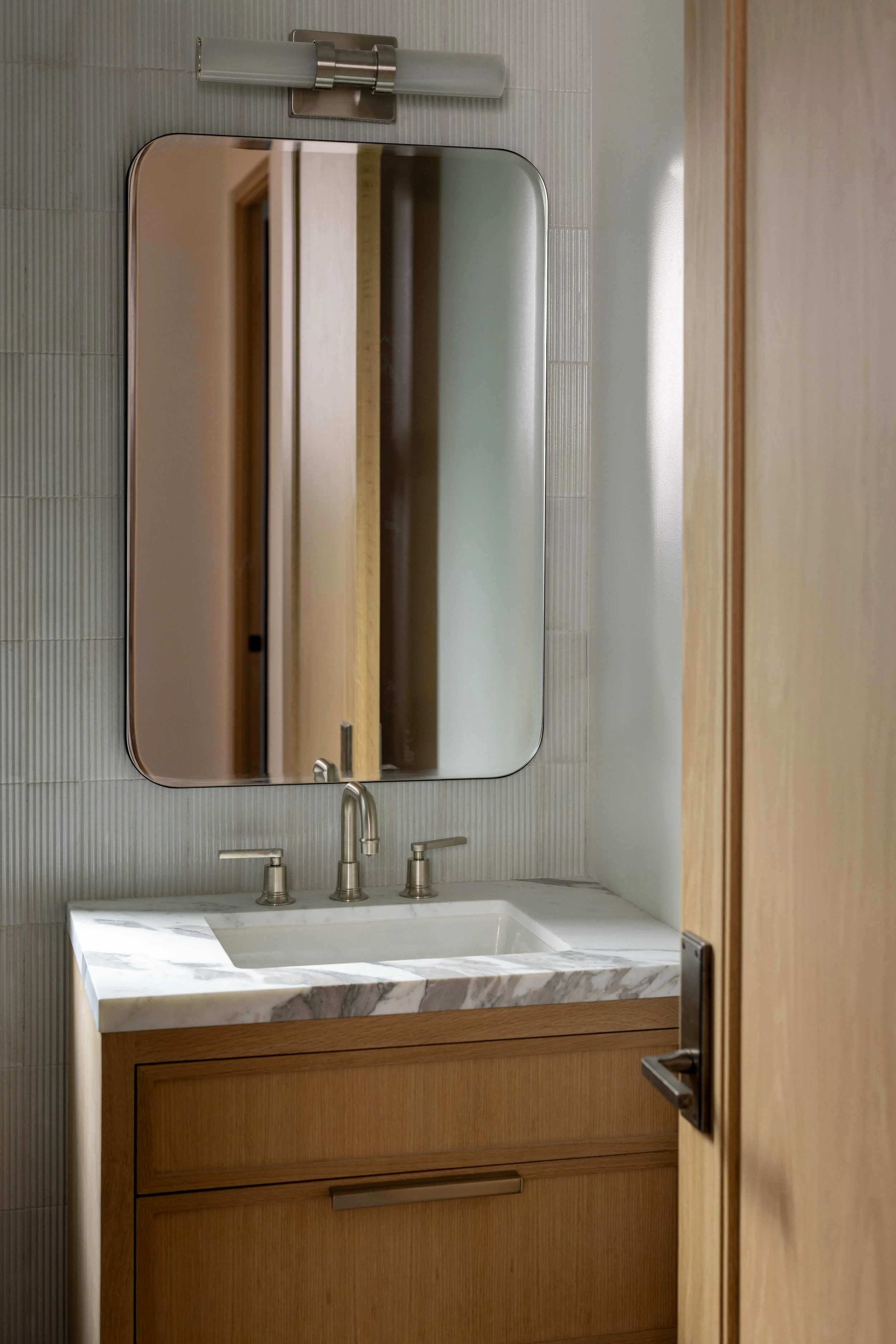 Bathroom with wooden cabinet, marble countertop, rectangular mirror, and wall-mounted light fixture.