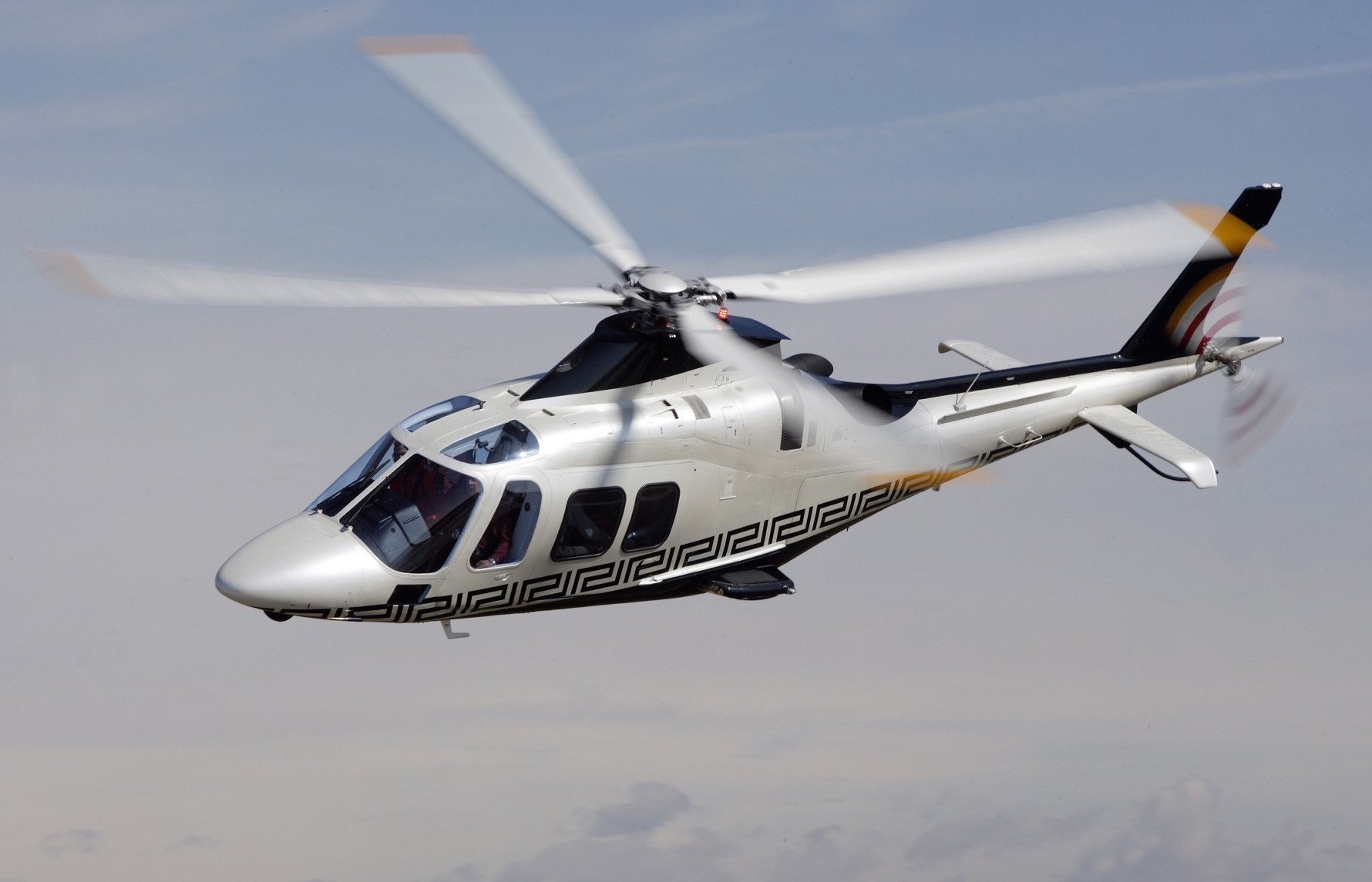 A white helicopter flying in the sky with a modern design and Greek key pattern along its side.