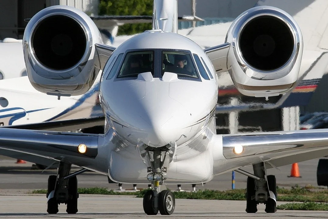 Front view of a white private jet aircraft on the tarmac with two jet engines, one on each wing.
