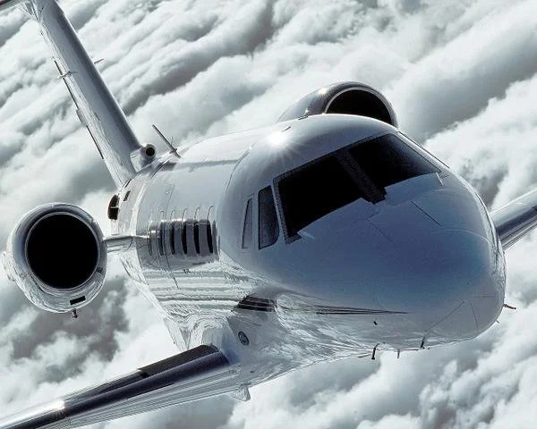 A sleek, silver private jet flying above the clouds.