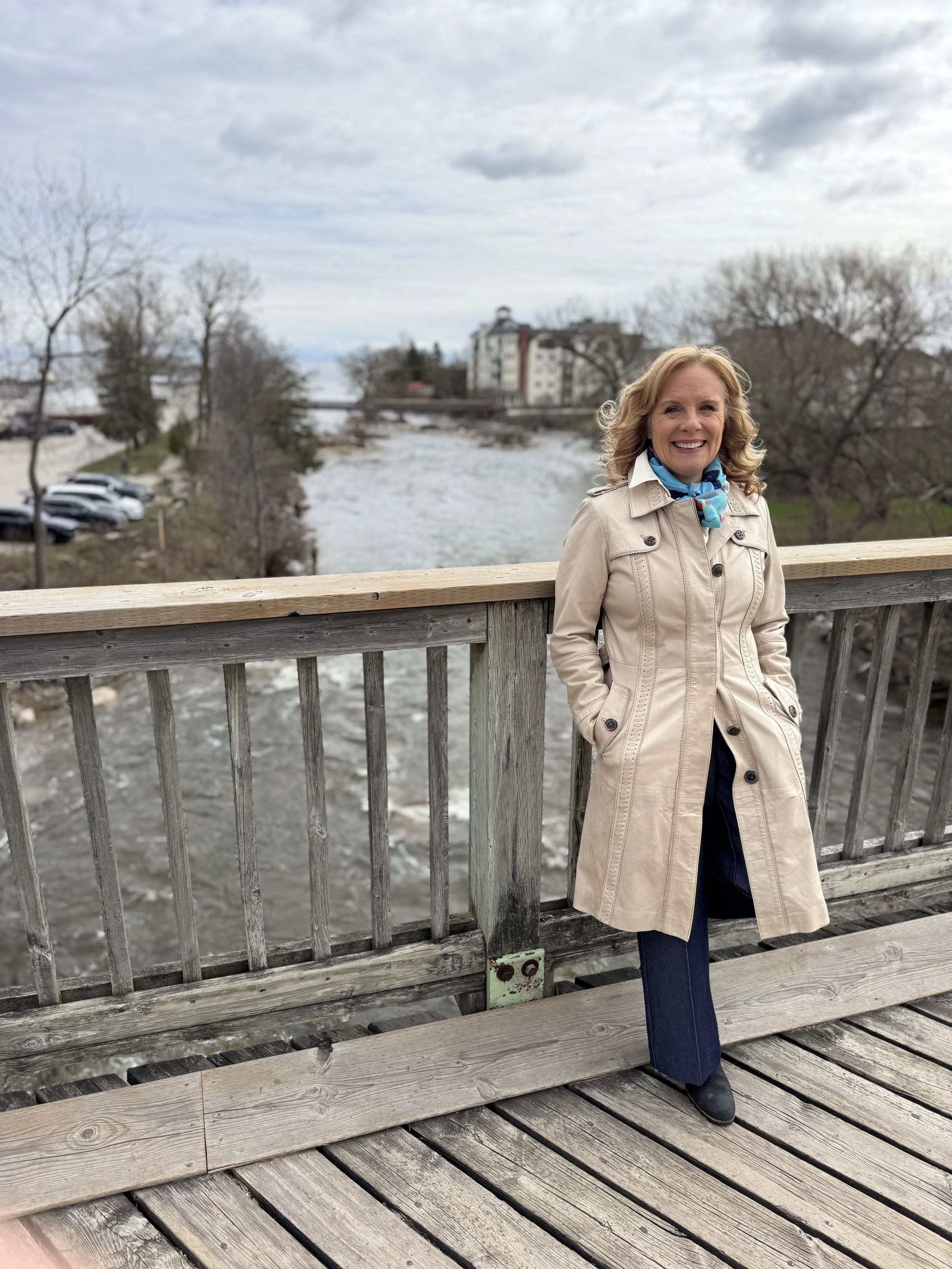 Mayoral Candidate Marni Moreau smiling on the Wooden Trestle Bridge in Thornbury, Ontario. Shows the Beaver River and Georgian Bay in the background.